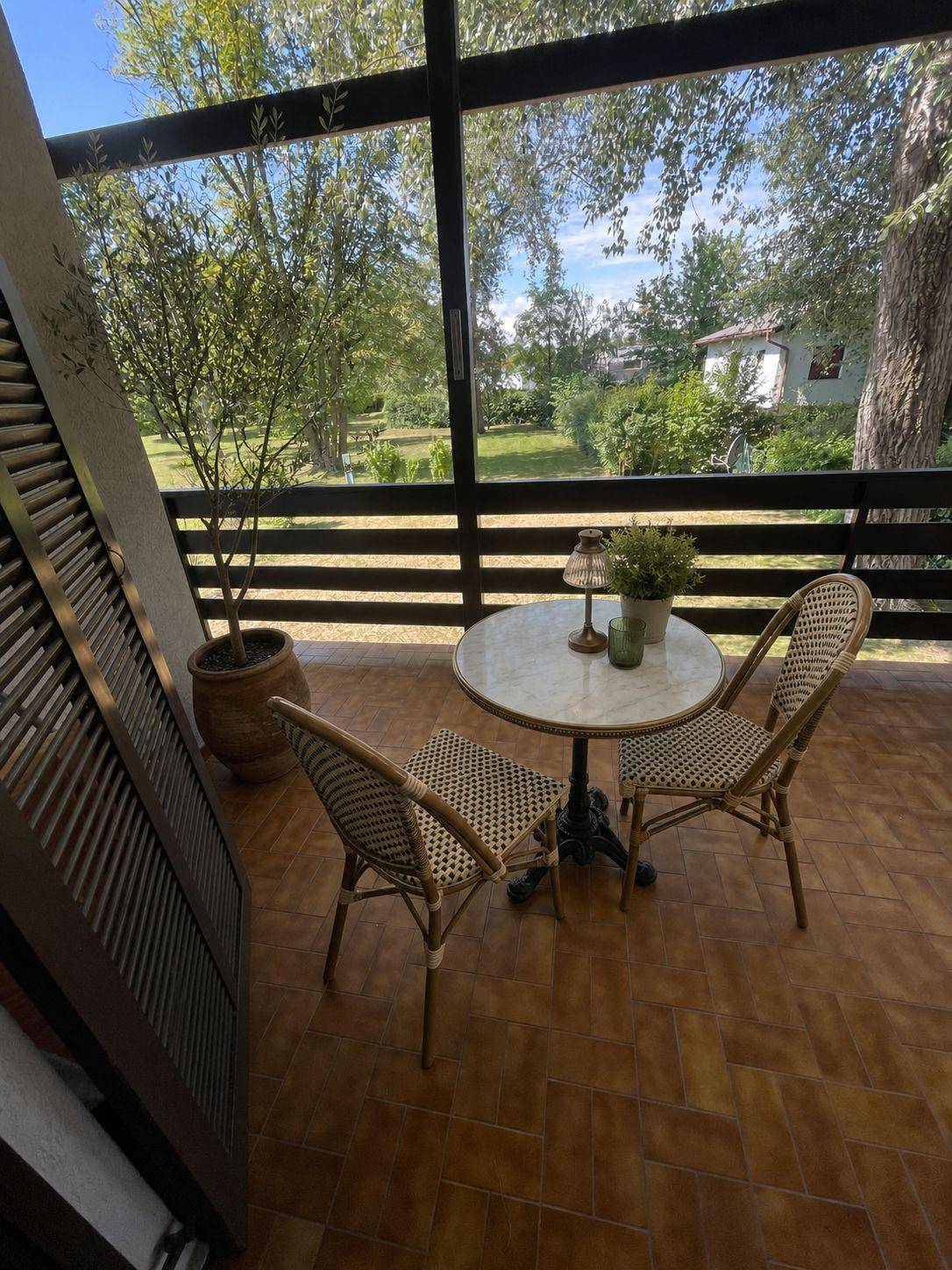 Möblierter Balkon mit Rattanmöbeln und Blick auf die grüne Umgebung unter blauem Himmel.