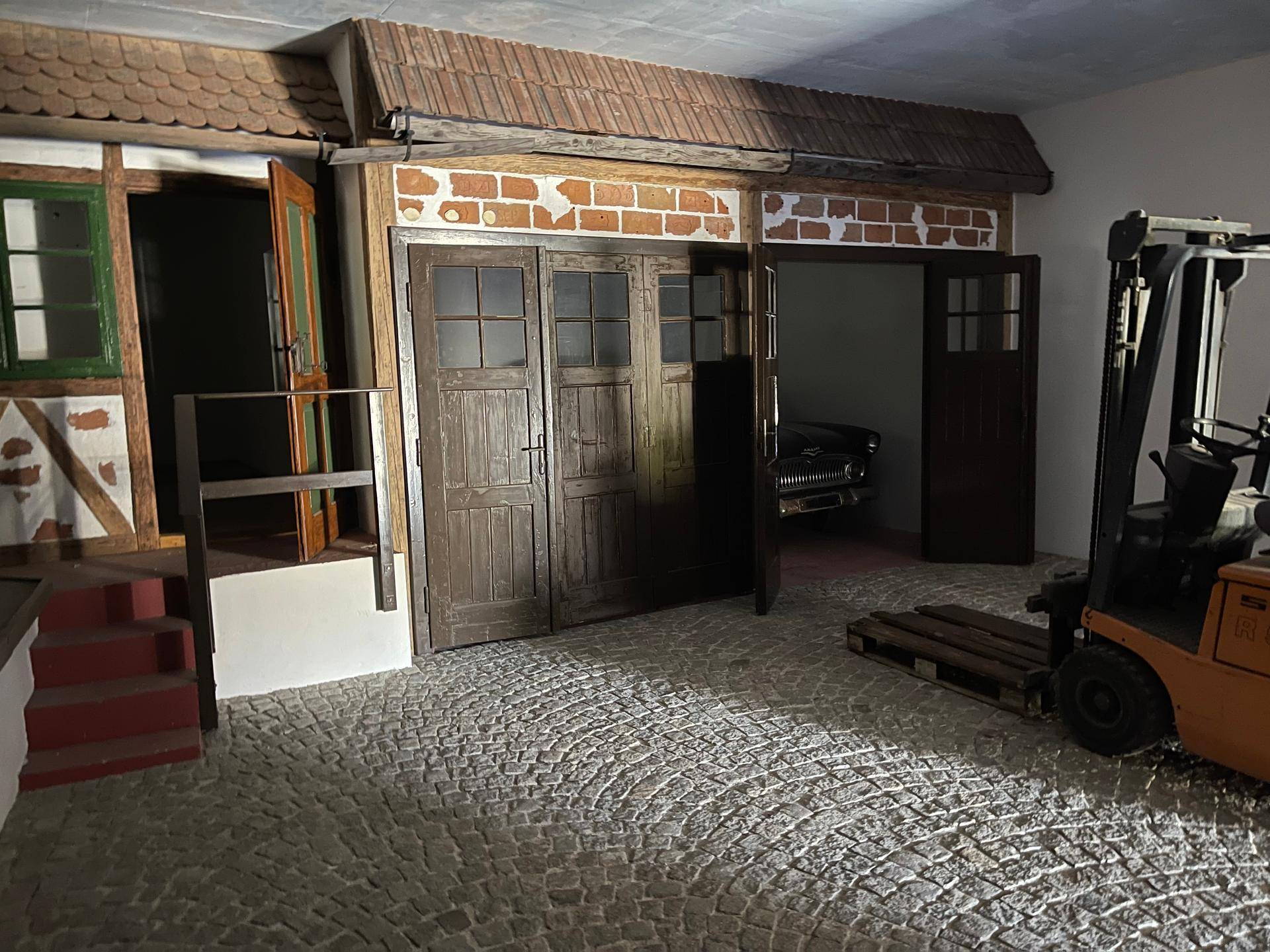 Thematischer Innenraum mit Kopfsteinpflasterboden, Gabelstapler und rustikalen Holztüren, die Garagen ähneln.