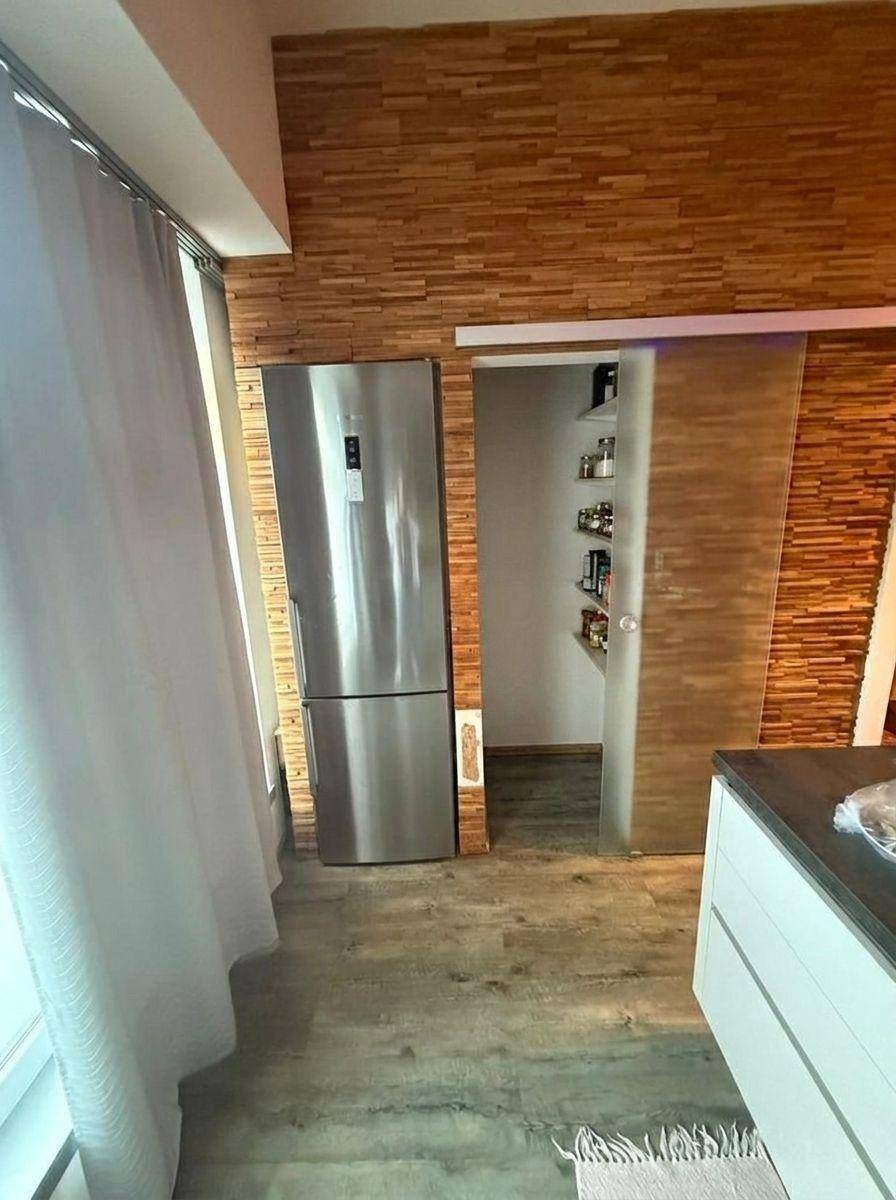 Küchenbereich mit großem Kühlschrank und Schiebetür, die zu einer praktischen Speisekammer führt.