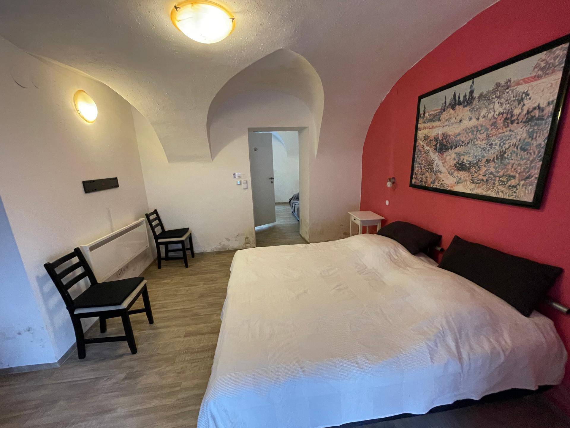 Schlafzimmer mit gewölbter Decke, roter Wand und Blick in einen weiteren Raum.