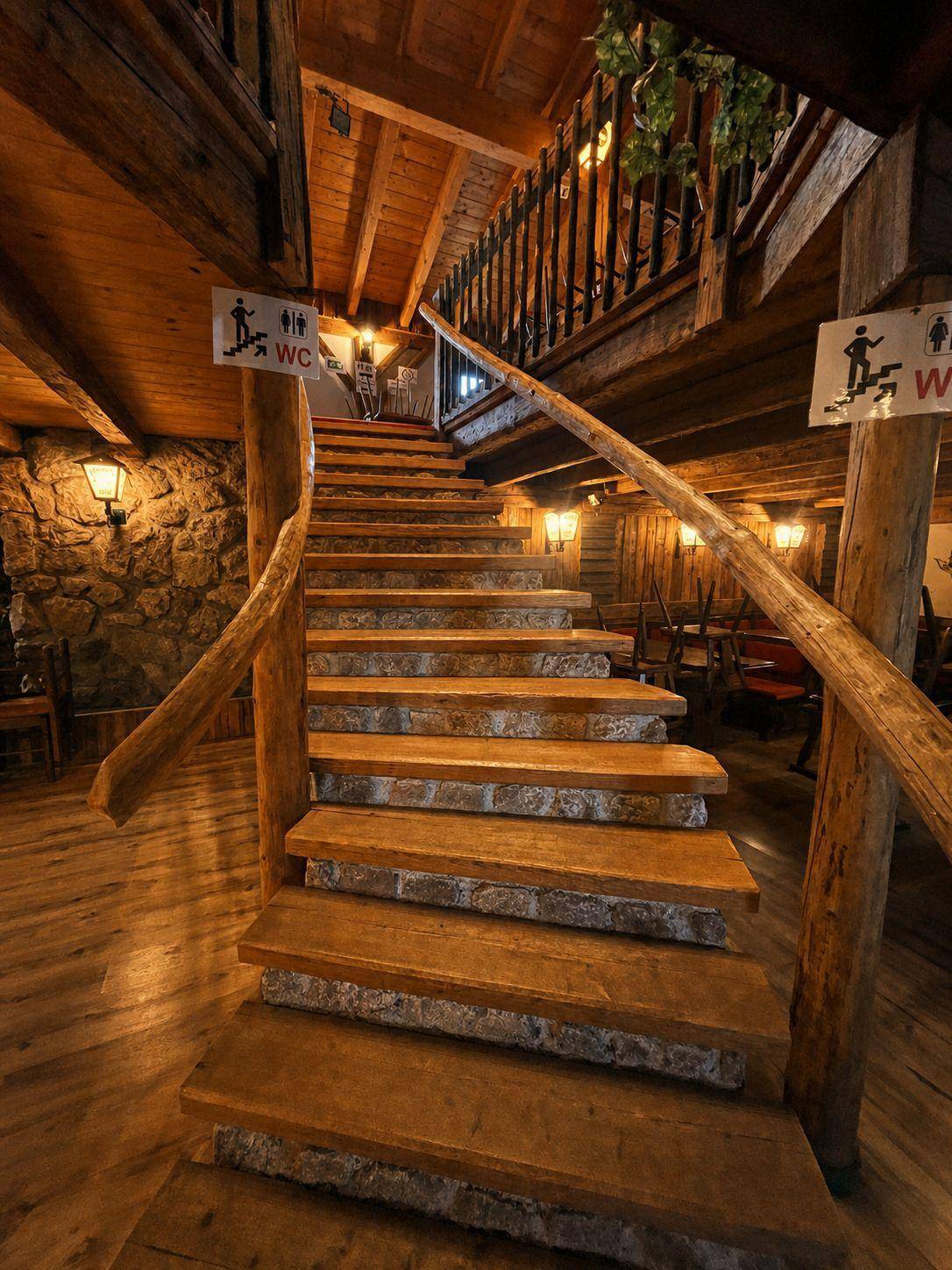 Geschwungene Holztreppe mit Steinakzenten und rustikalen Wandleuchten, die nach oben führt und einladend wirkt.