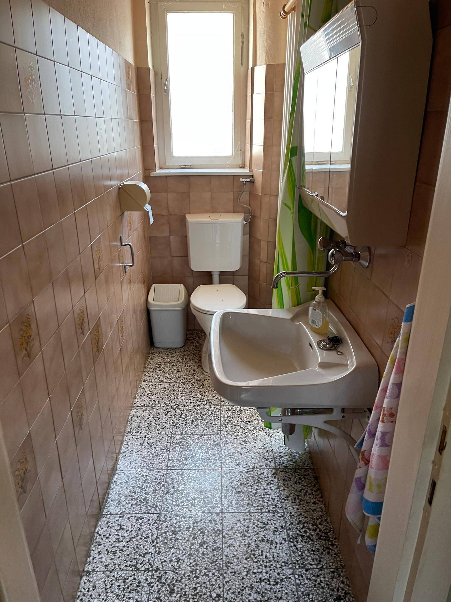 Kleines WC mit Fliesenboden, Fenster und einfacher Ausstattung.