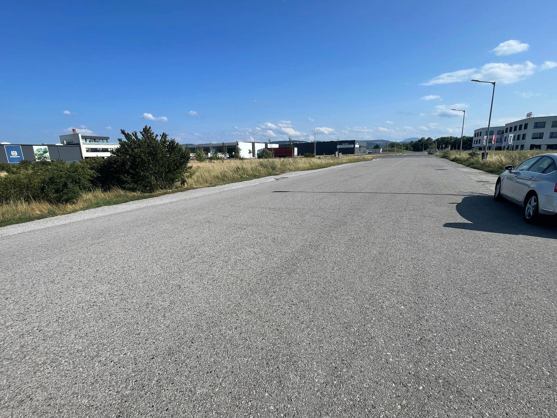 Eine asphaltierte Straße führt durch ein Gewerbegebiet mit modernen Gebäuden unter klarem blauem Himmel.
