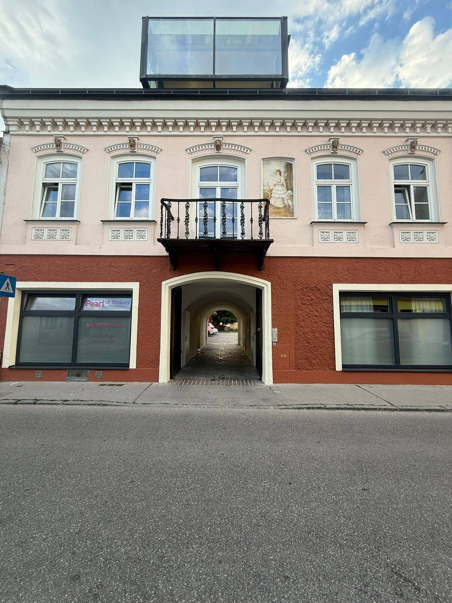Historische Fassade eines Altbaus mit französischem Balkon und moderner Glasstruktur auf dem Dach.
