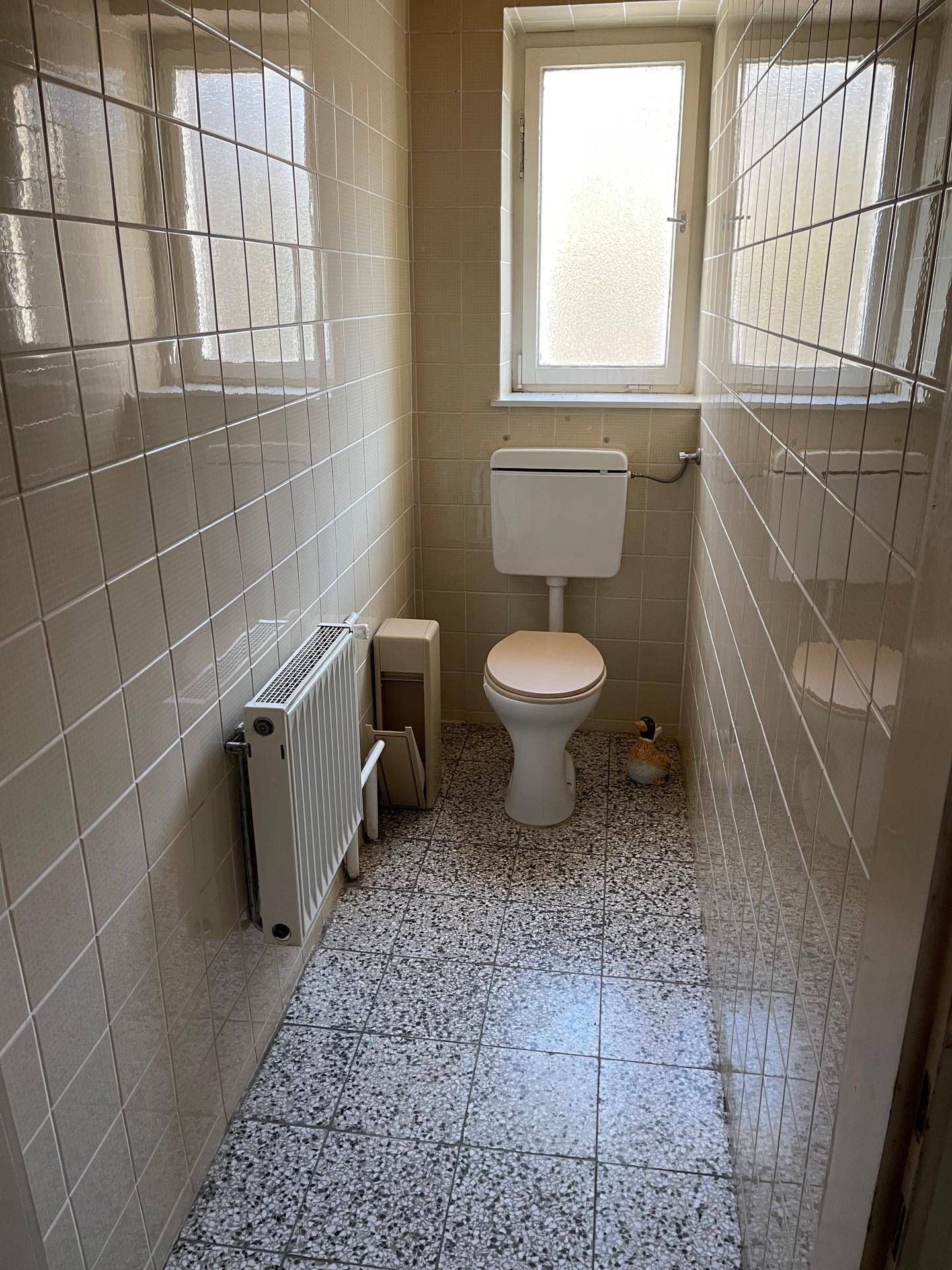 WC mit beigen Fliesen, Toilette und Fenster.