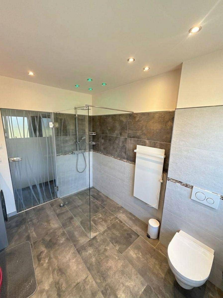 Geräumiges Badezimmer mit begehbarer Dusche, wandhängendem WC und modernen Fliesen.
