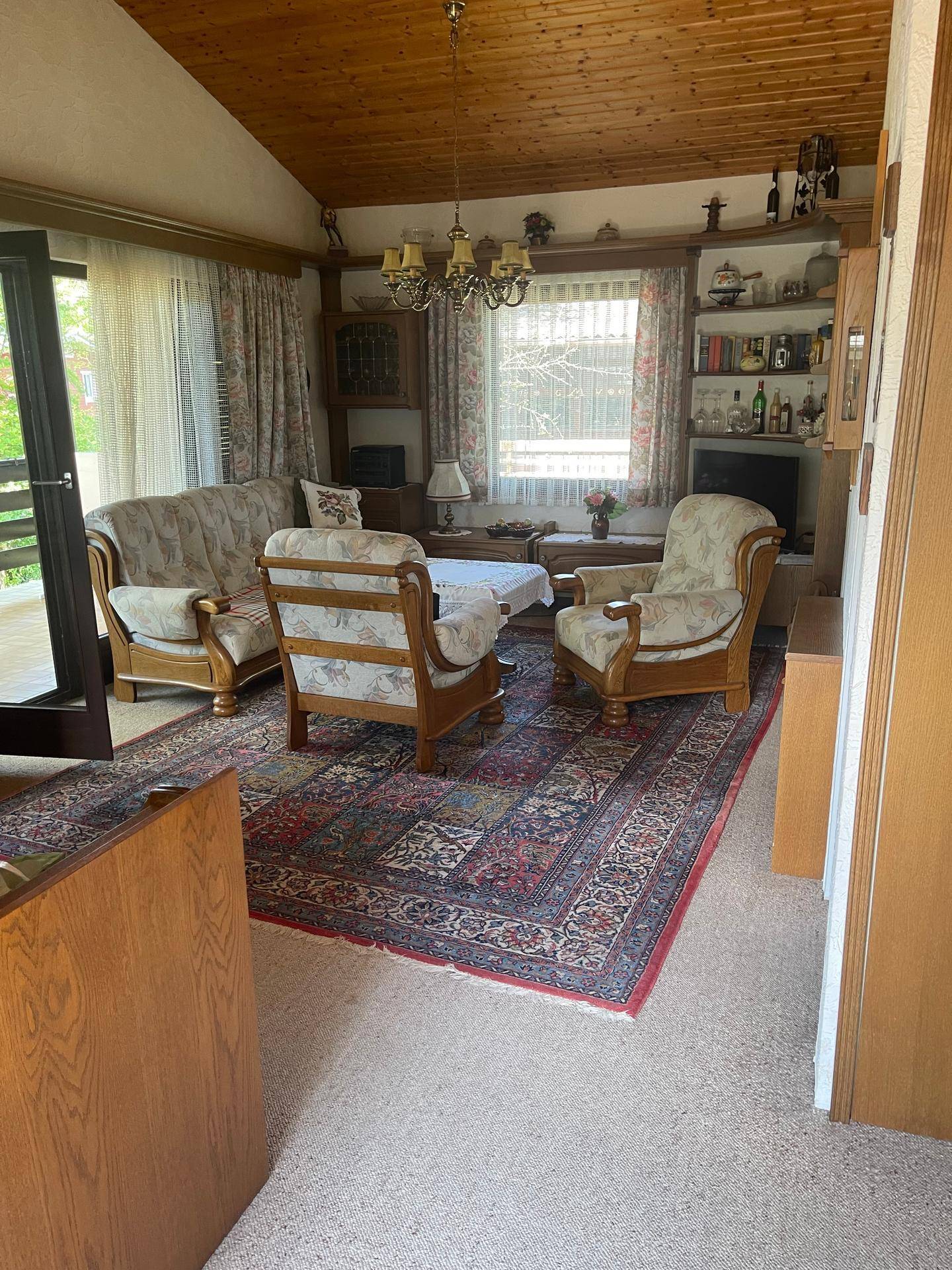Gemütliches Wohnzimmer mit Holzbalkendecke, traditionellen Möbeln und einem großen Teppich.