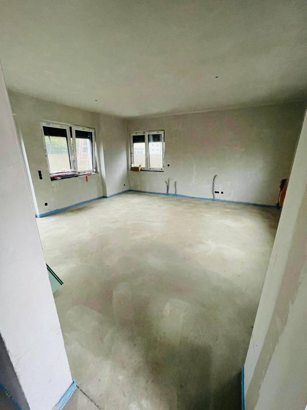 Geräumiger Rohbau-Raum mit Estrichboden und mehreren Fenstern, bereit für den Innenausbau.