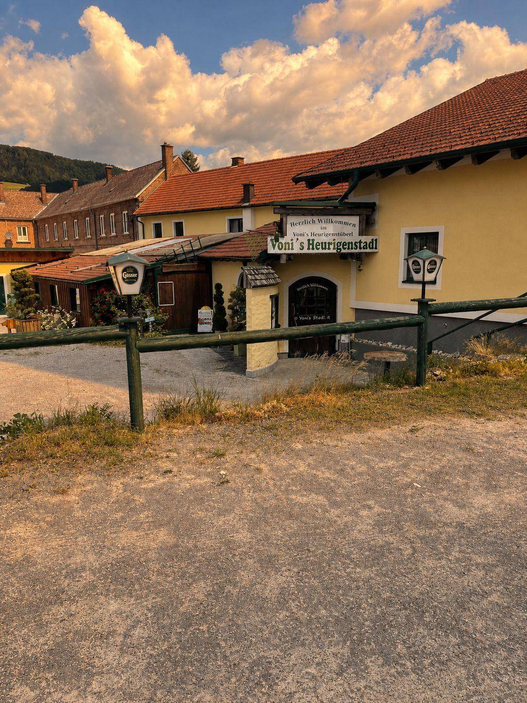 Eingangsbereich des Heurigenstadls mit traditionellen Laternen und Holzzaun in ländlicher Umgebung.