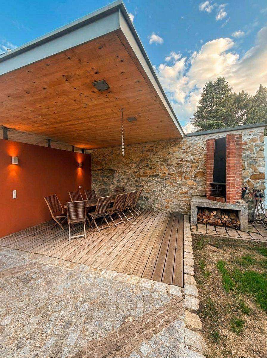 Gemütlicher Außenbereich mit Holzdielen, großem Esstisch und integriertem Grill, umgeben von einer Steinmauer.