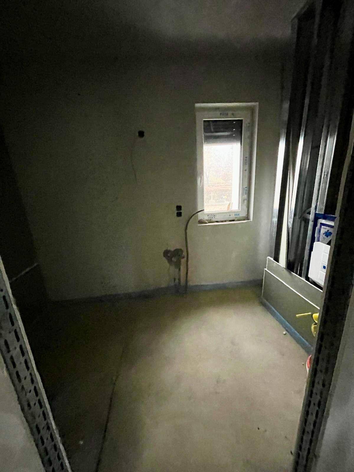Kleiner Rohbau-Raum mit Estrichboden und Fenster, vorbereitet für Installationen.