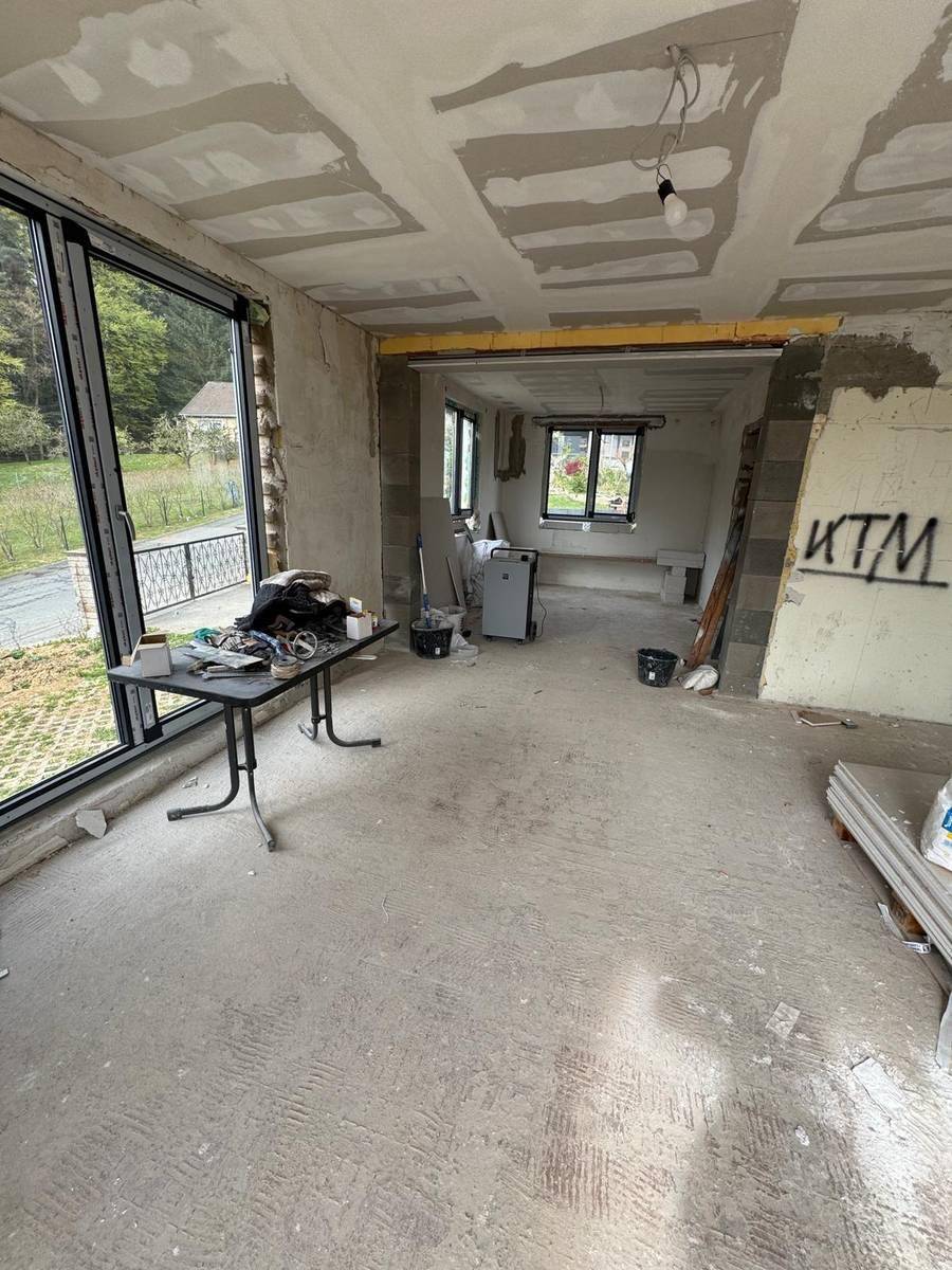 Großer Wohnbereich im Rohbau mit großen Schiebetüren und Blick ins Grüne, bereit für den Innenausbau.