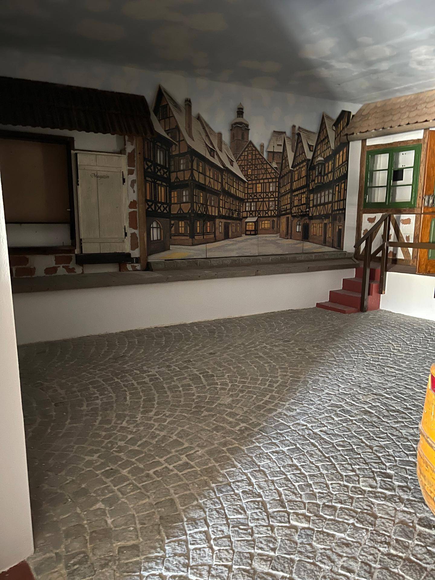 Thematischer Innenraum mit Kopfsteinpflasterboden und einer Wandmalerei, die eine historische Stadtansicht darstellt.