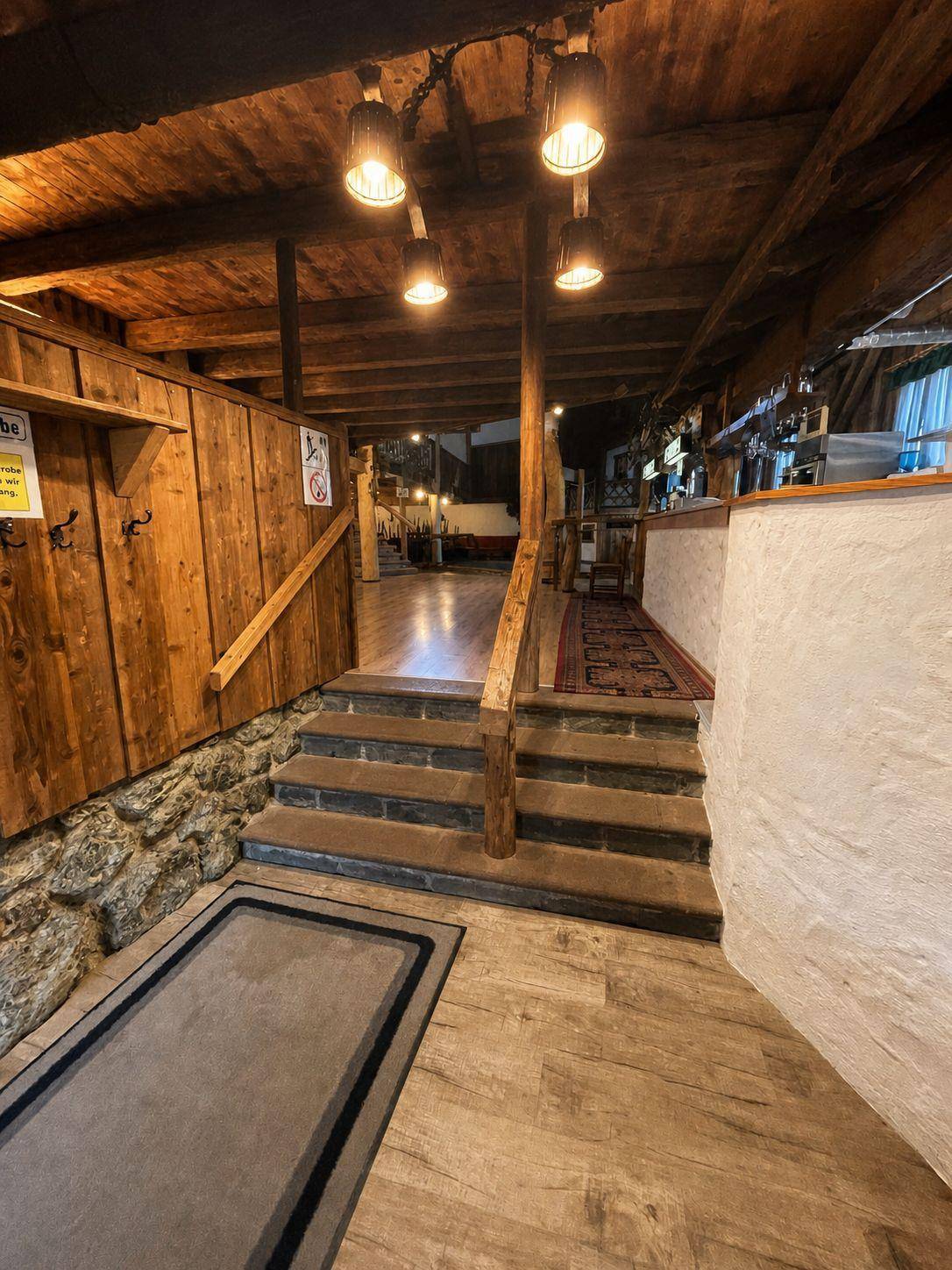 Treppenaufgang mit Holzgeländer und Steinmauer, der zu einem oberen Bereich führt und rustikal wirkt.