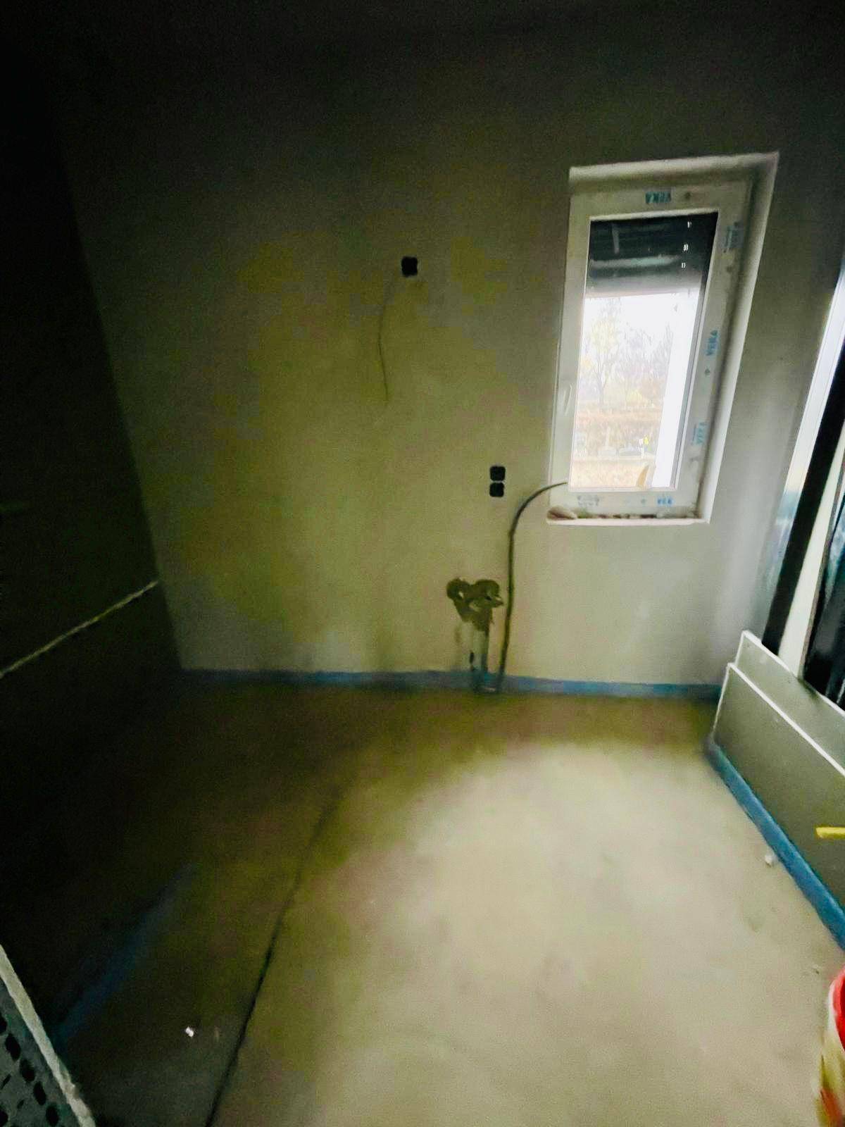 Kleiner Rohbau-Raum mit Estrichboden und Fenster, vorbereitet für Installationen.