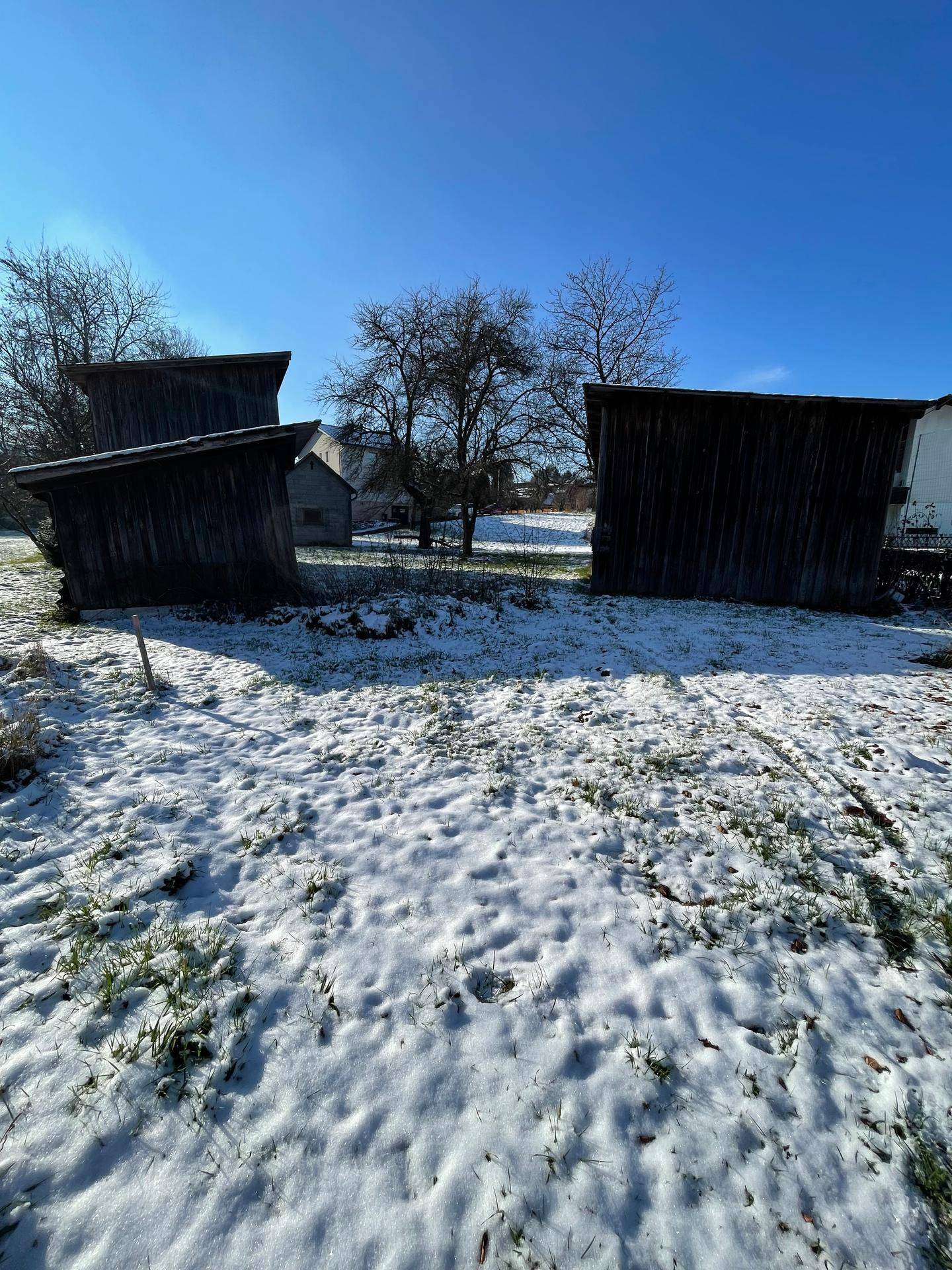 Winterlicher Garten mit mehreren Holzschuppen und schneebedecktem Rasen unter blauem Himmel.