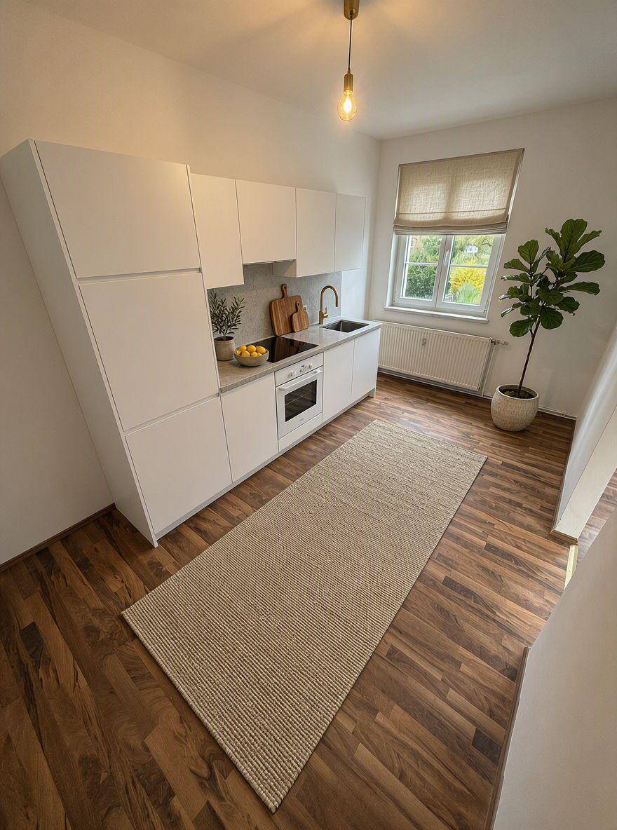 Moderne Küche mit weißen Schränken, Holzboden und Blick ins Grüne durch das Fenster.