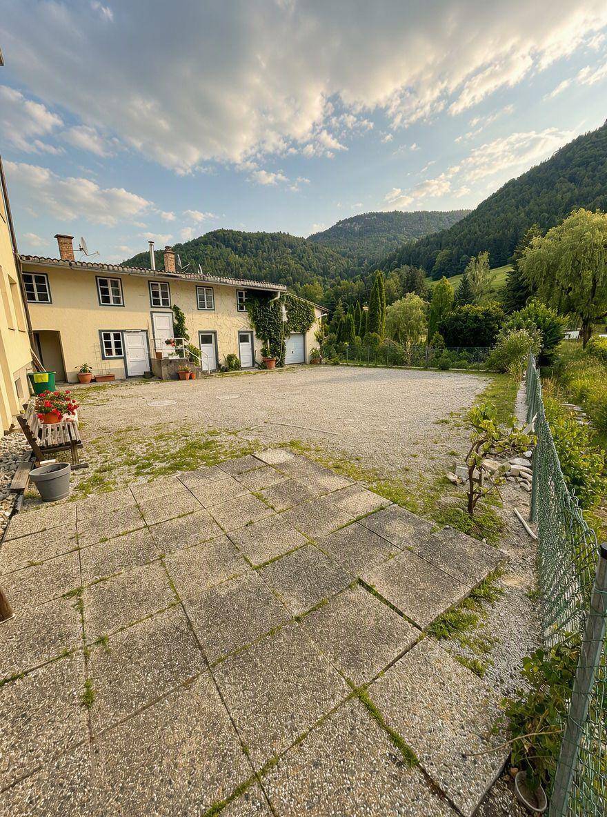Hinterhof mit großer gepflasterter Terrasse und Blick auf die grüne Umgebung.