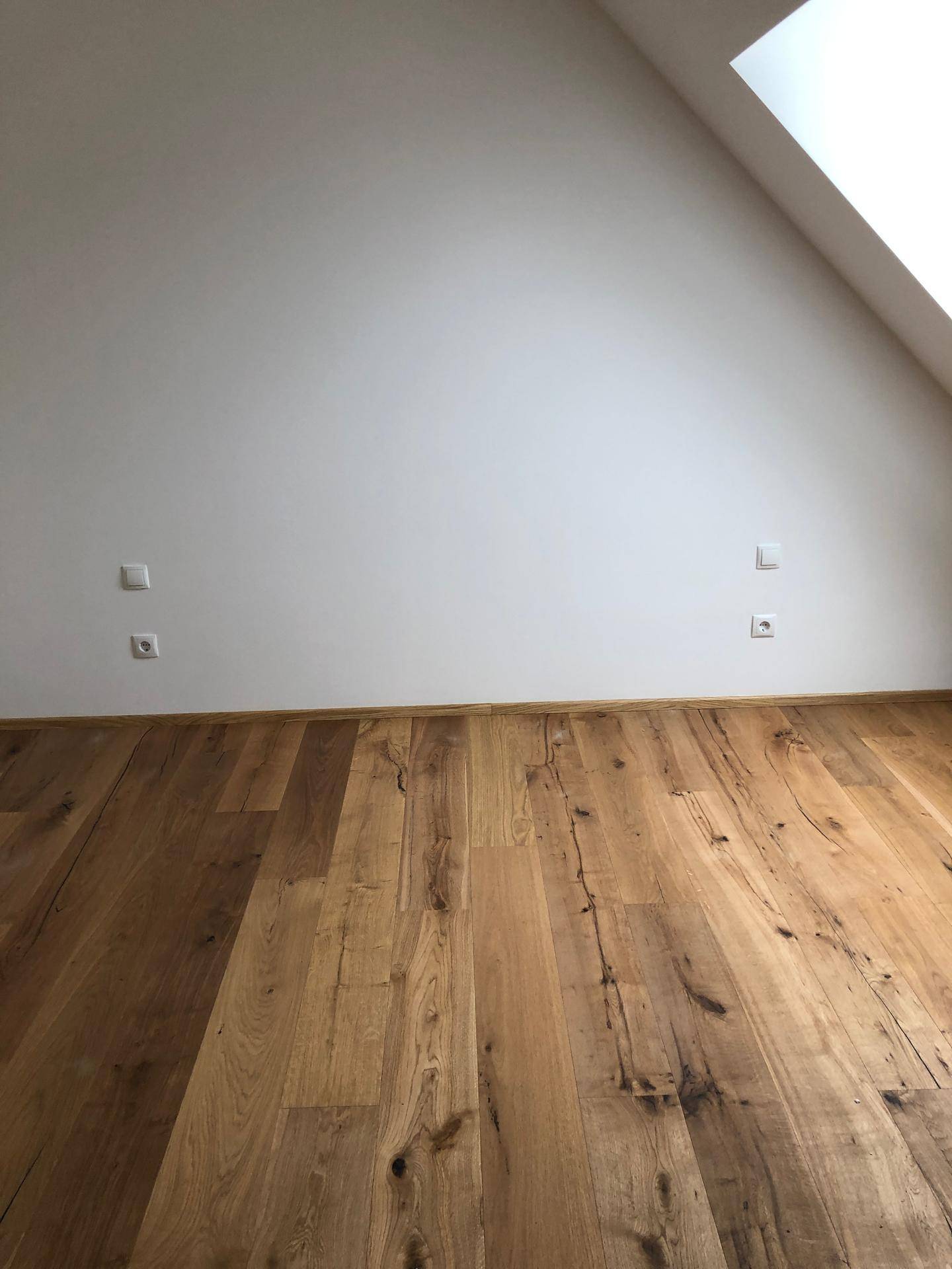 Geräumiges Zimmer im Dachgeschoss mit Holzboden und schräger Wand unter einem Dachfenster.