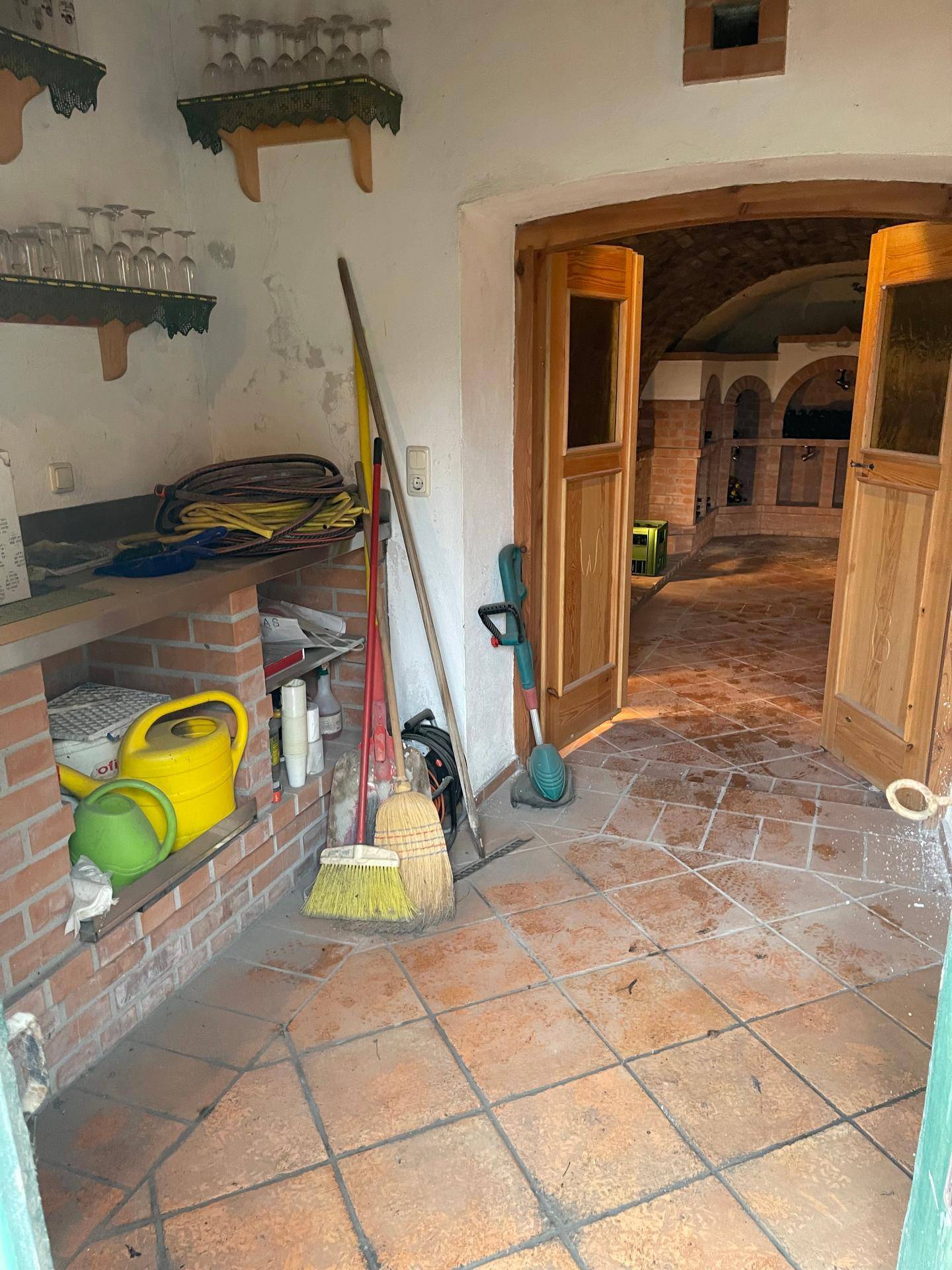 Abstellraum mit Terrakottaboden und Ziegelregalen, gefüllt mit Reinigungsgeräten und Gartenzubehör, angrenzend an den Weinkeller.