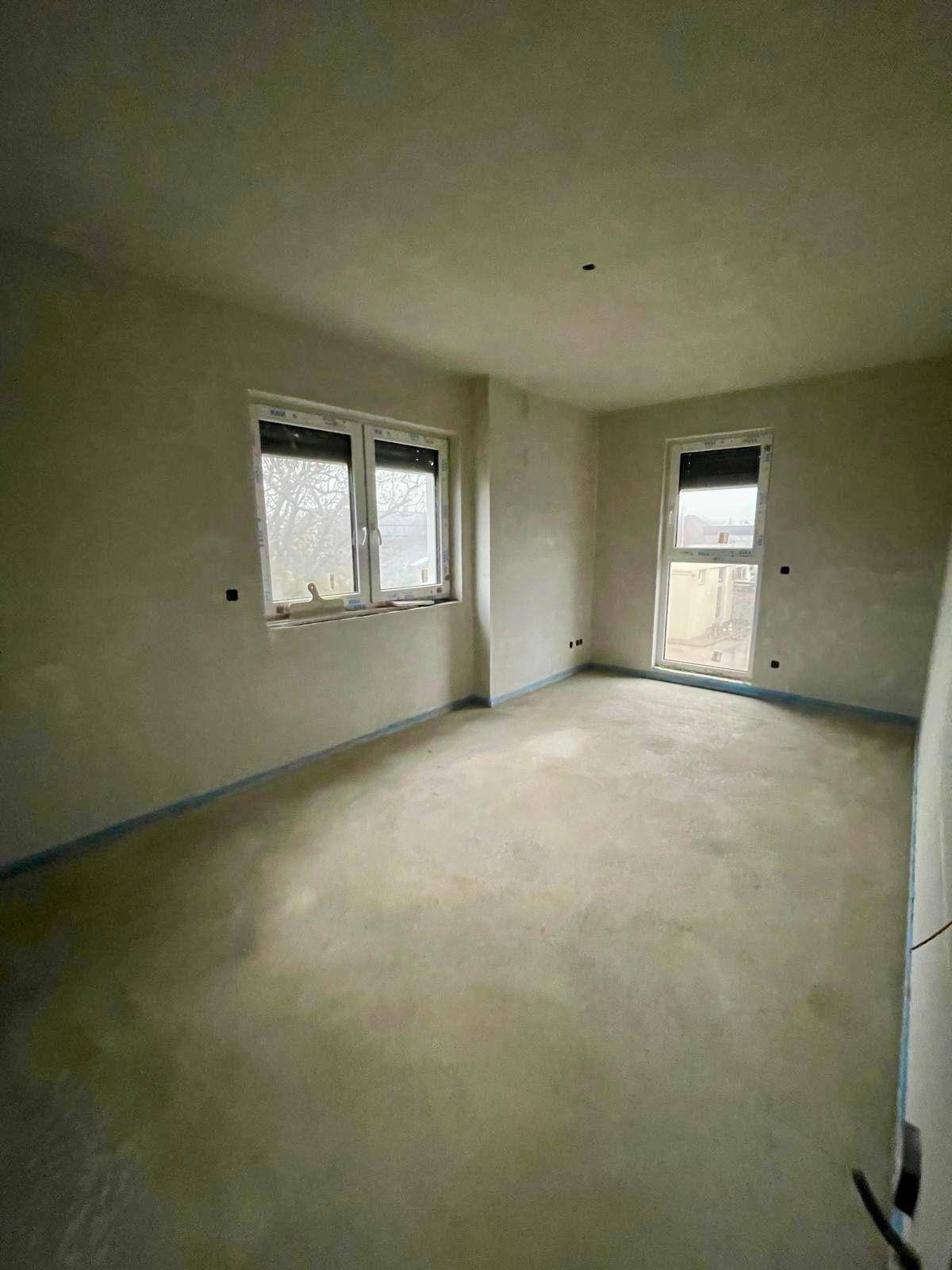 Rohbau-Zimmer mit Estrichboden und zwei Fenstern, bereit für die Fertigstellung.