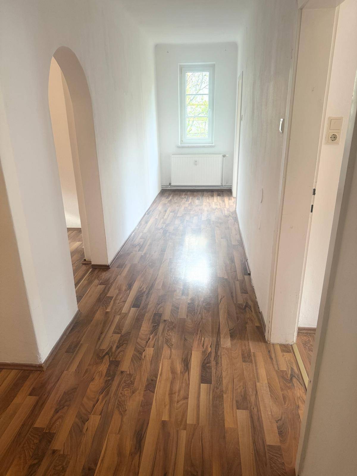 Leerer Flur mit Holzboden und einem Fenster, das natürliches Licht hereinlässt.