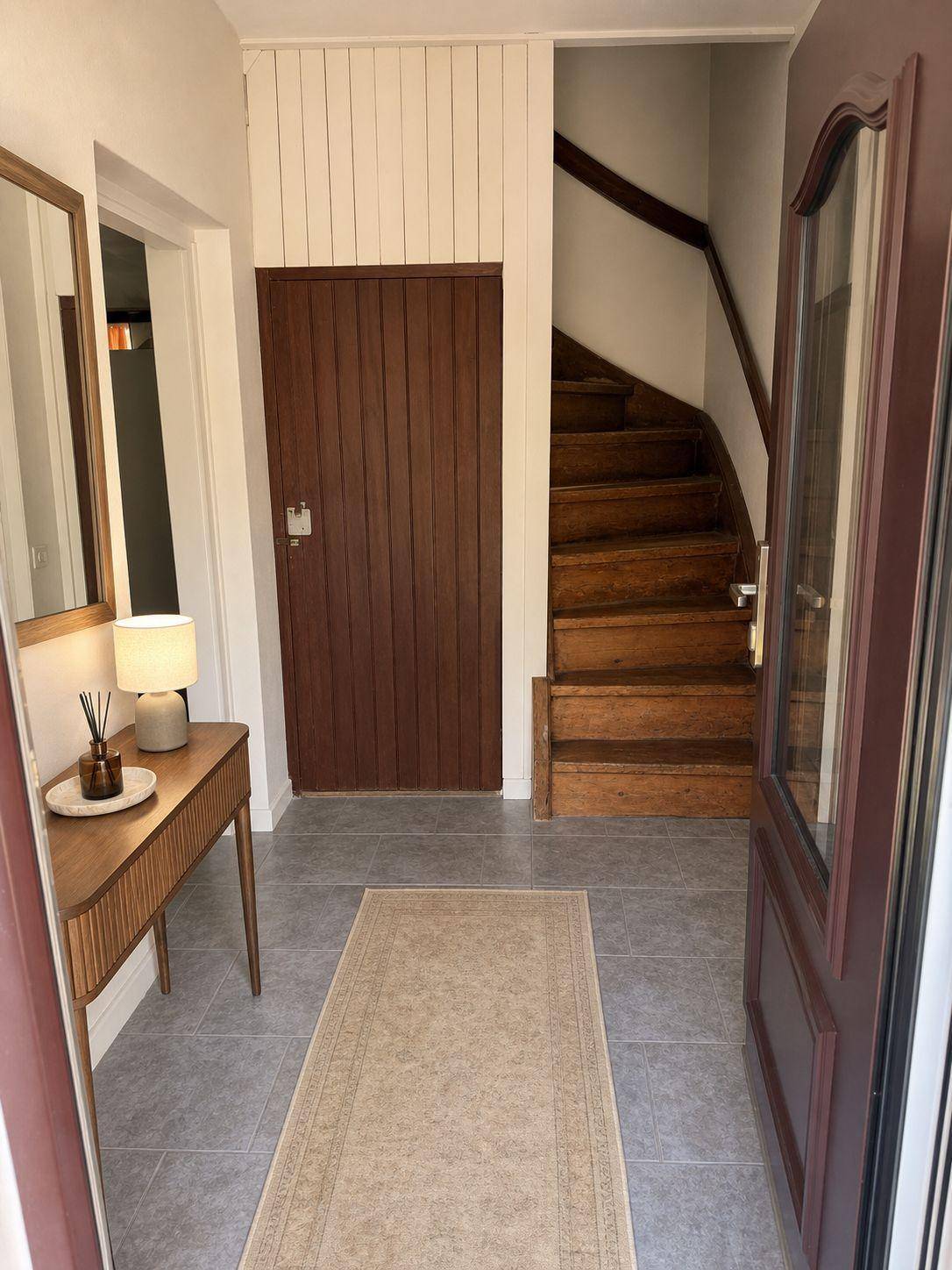 Heller Eingangsbereich mit Fliesenboden, Holztreppe und modernem Konsolentisch.