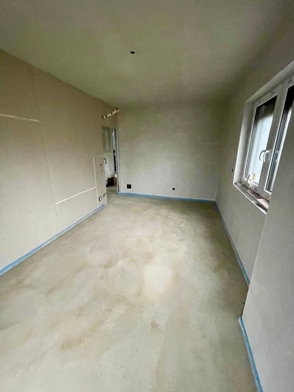Geräumiger Rohbau-Raum mit Estrichboden und Fenster, bereit für den Innenausbau.