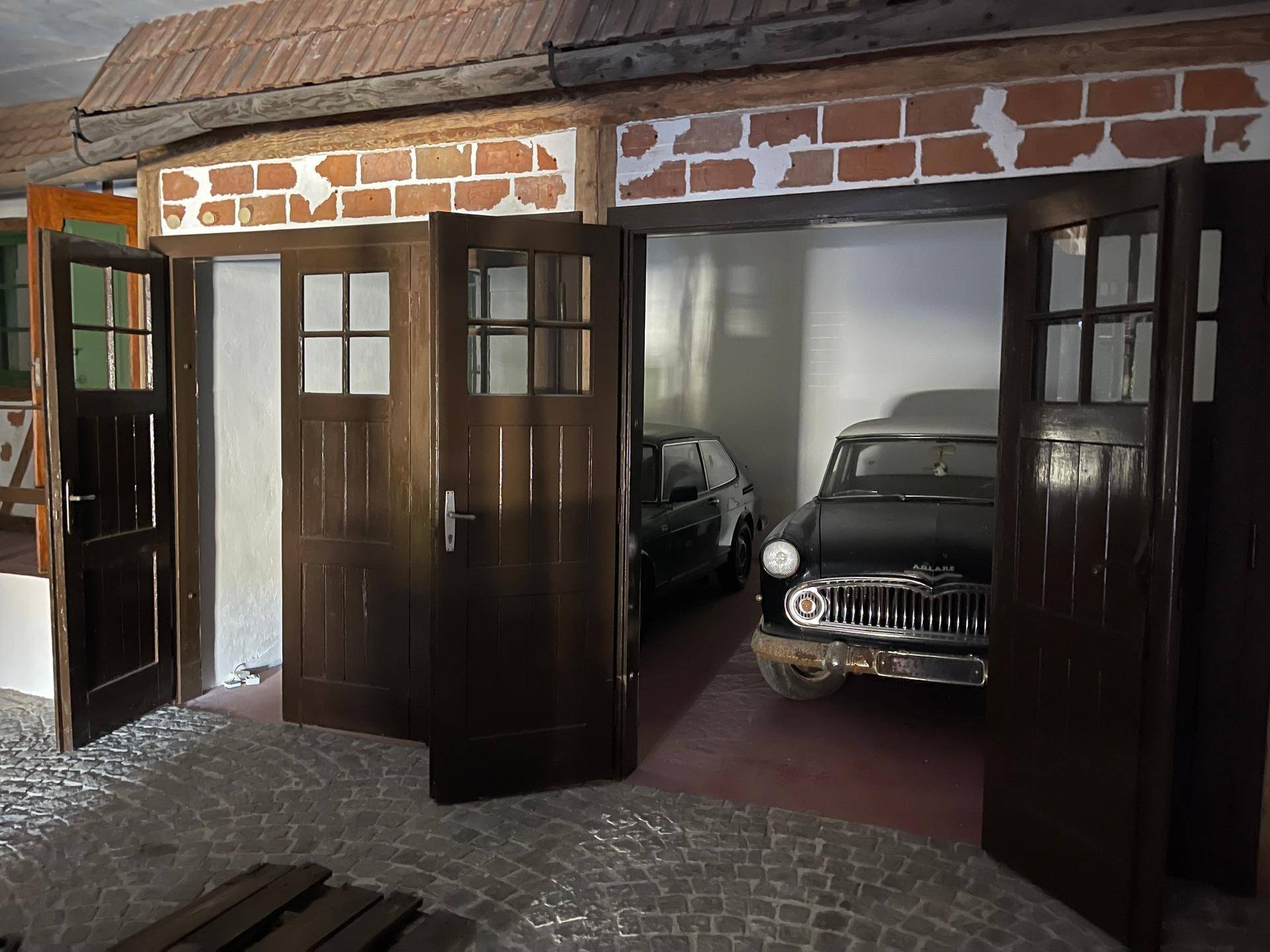 Thematischer Innenraum mit rustikalen Holztüren, die den Blick auf Oldtimer in einer Garage freigeben.