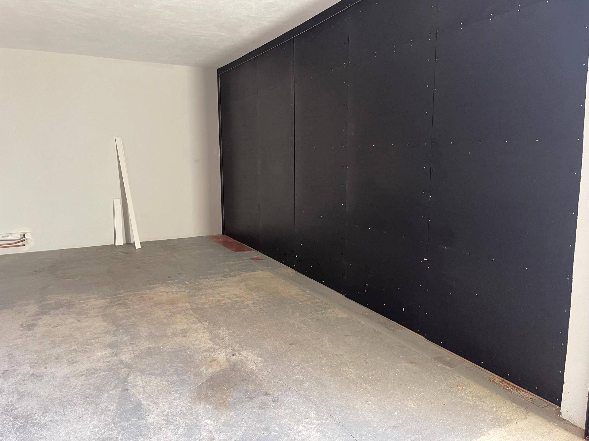 Langer Garagenraum mit dunkler Seitenwand und schmutzigem Betonboden, der Renovierungsarbeiten erfordert.