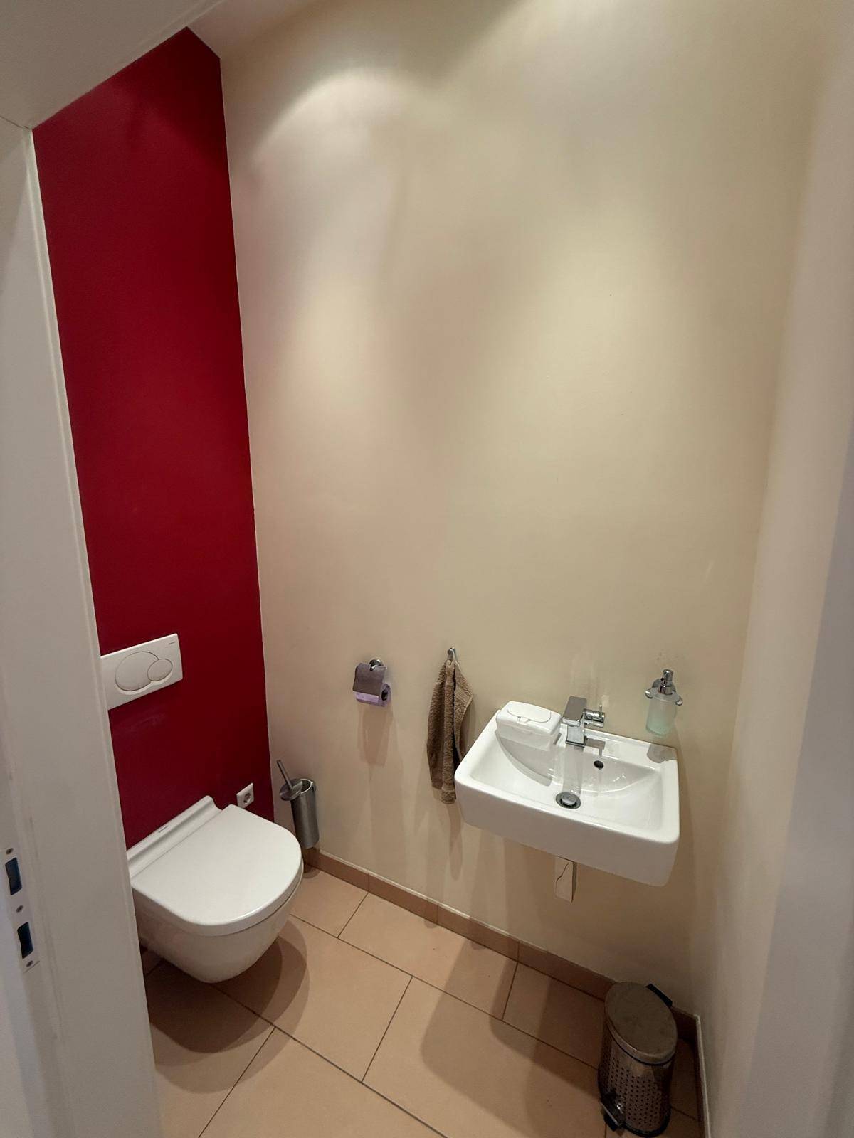 Modernes Gäste-WC mit wandhängender Toilette und kleinem Waschbecken, akzentuiert durch eine rote Wand.