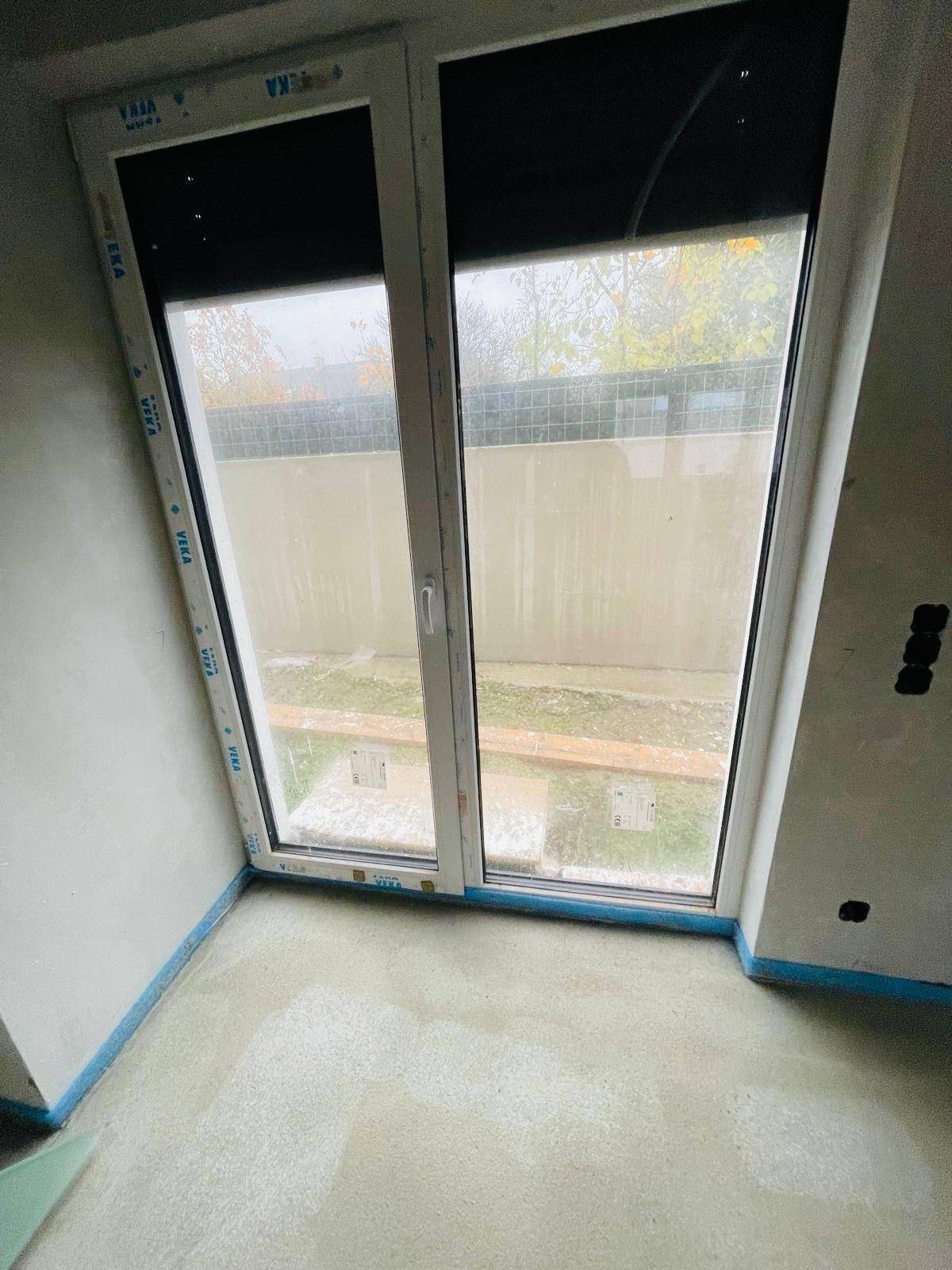 Rohbau-Zimmer mit großem Fenster und Blick auf den Gartenbereich.