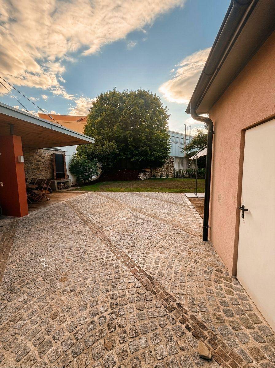 Gepflasterter Innenhof mit Zufahrt, der zu einem grünen Gartenbereich mit altem Baumbestand führt.