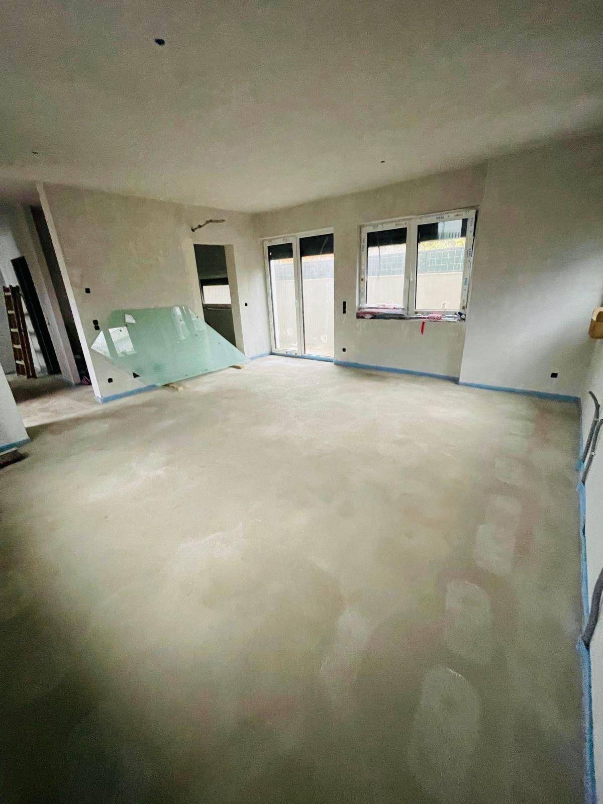 Geräumiger Rohbau-Raum mit Estrichboden und großen Fenstern, bereit für den Innenausbau.