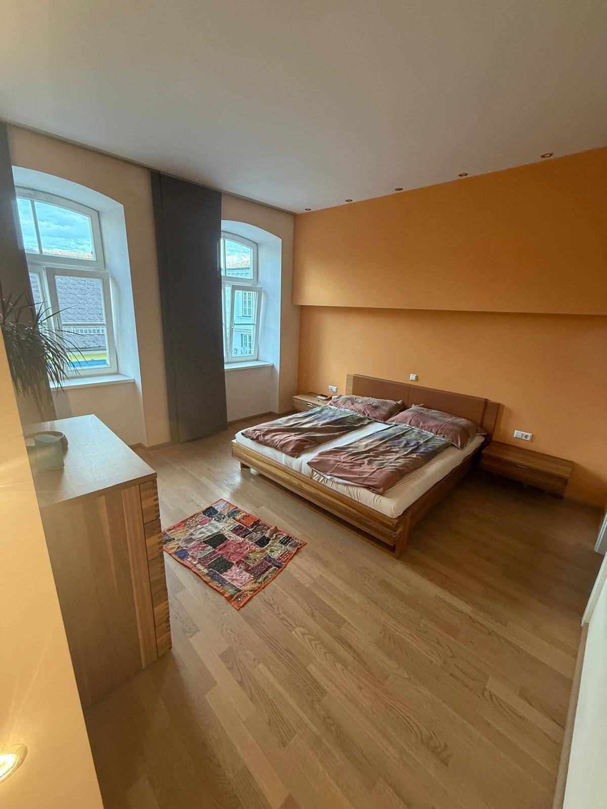 Geräumiges Schlafzimmer mit Holzboden, großem Doppelbett und orangefarbener Akzentwand.