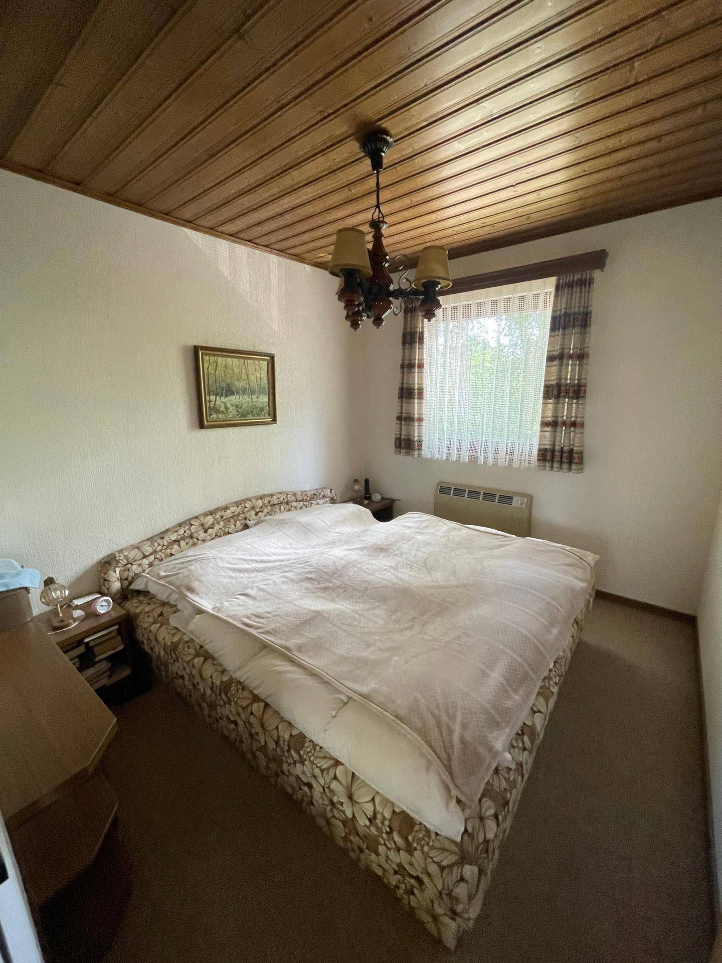 Traditionelles Schlafzimmer mit Holzbalkendecke, Doppelbett und gemusterten Vorhängen.