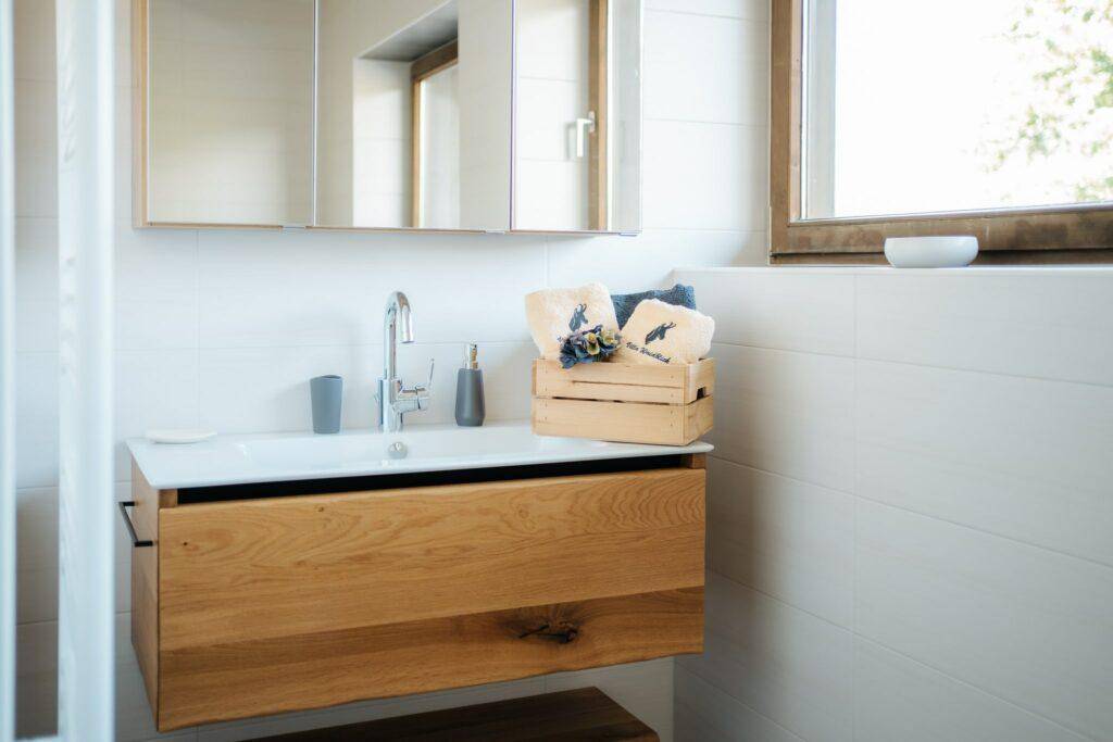 Helles Badezimmer mit Holzwaschtisch, Spiegelschrank und Fenster, das natürliches Licht spendet.