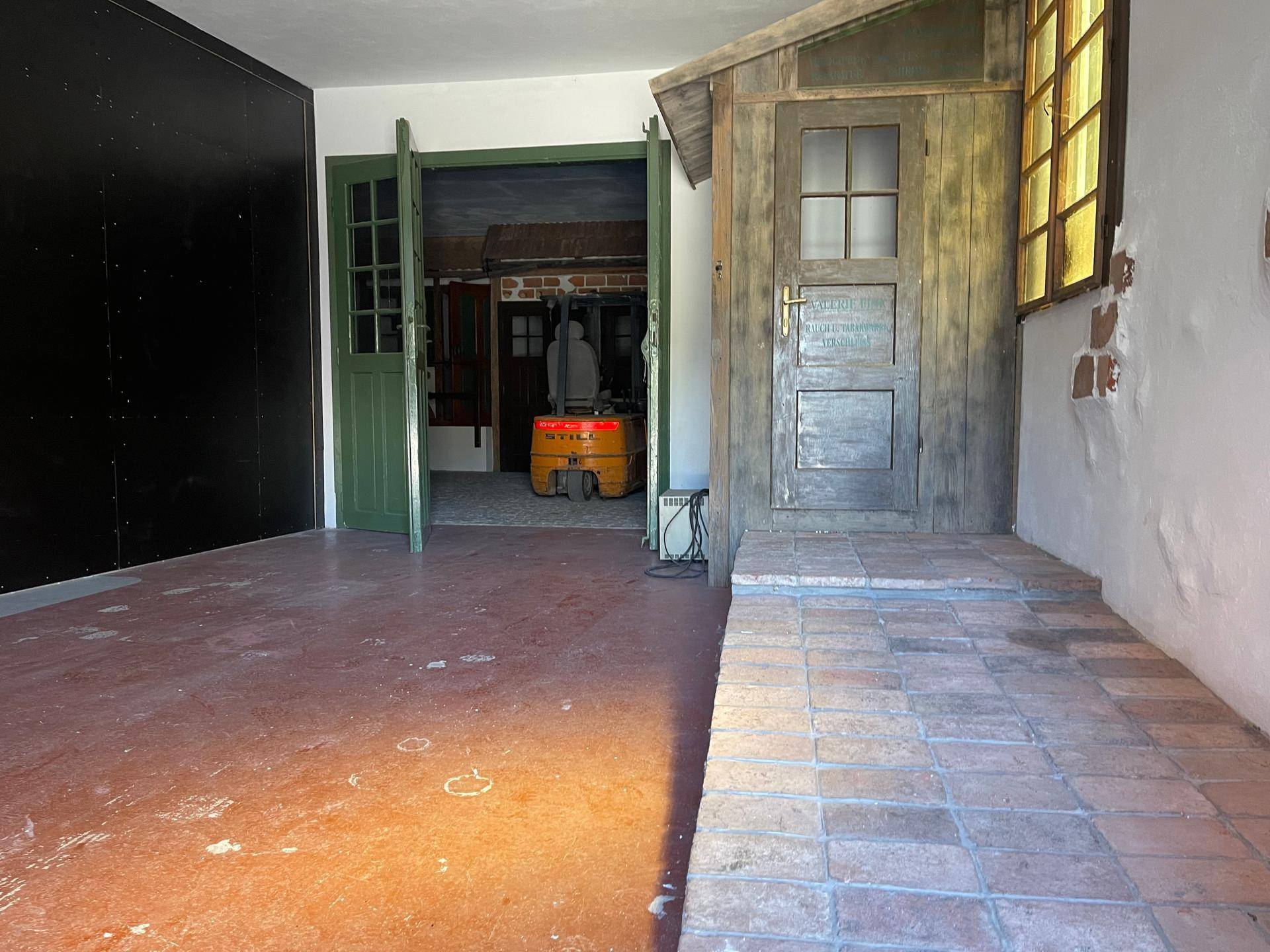 Innenraum mit Ziegelfliesenrampe, einer kleinen Holzhütte und einem Gabelstapler im Hintergrund.