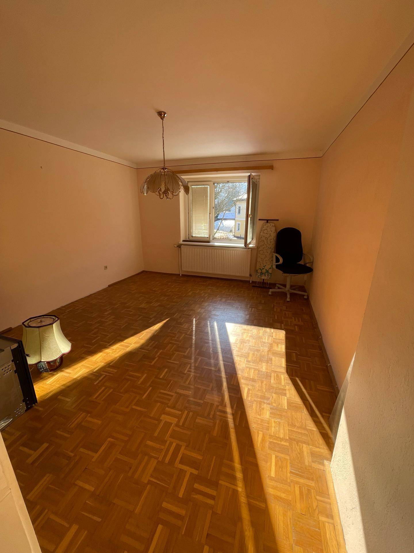 Geräumiges Wohnzimmer mit Parkettboden, Fenster und viel Sonnenlicht.