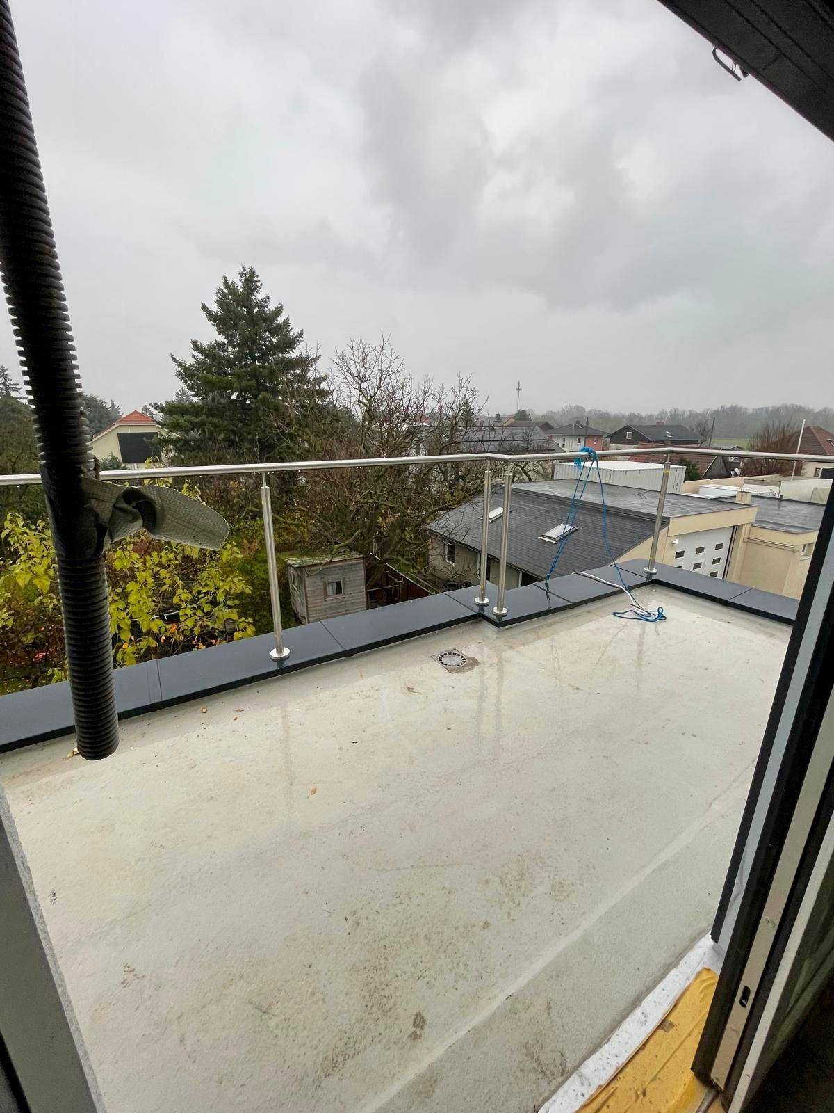 Geräumige Terrasse mit Glasgeländer und weitem Blick über die umliegende Wohngegend.