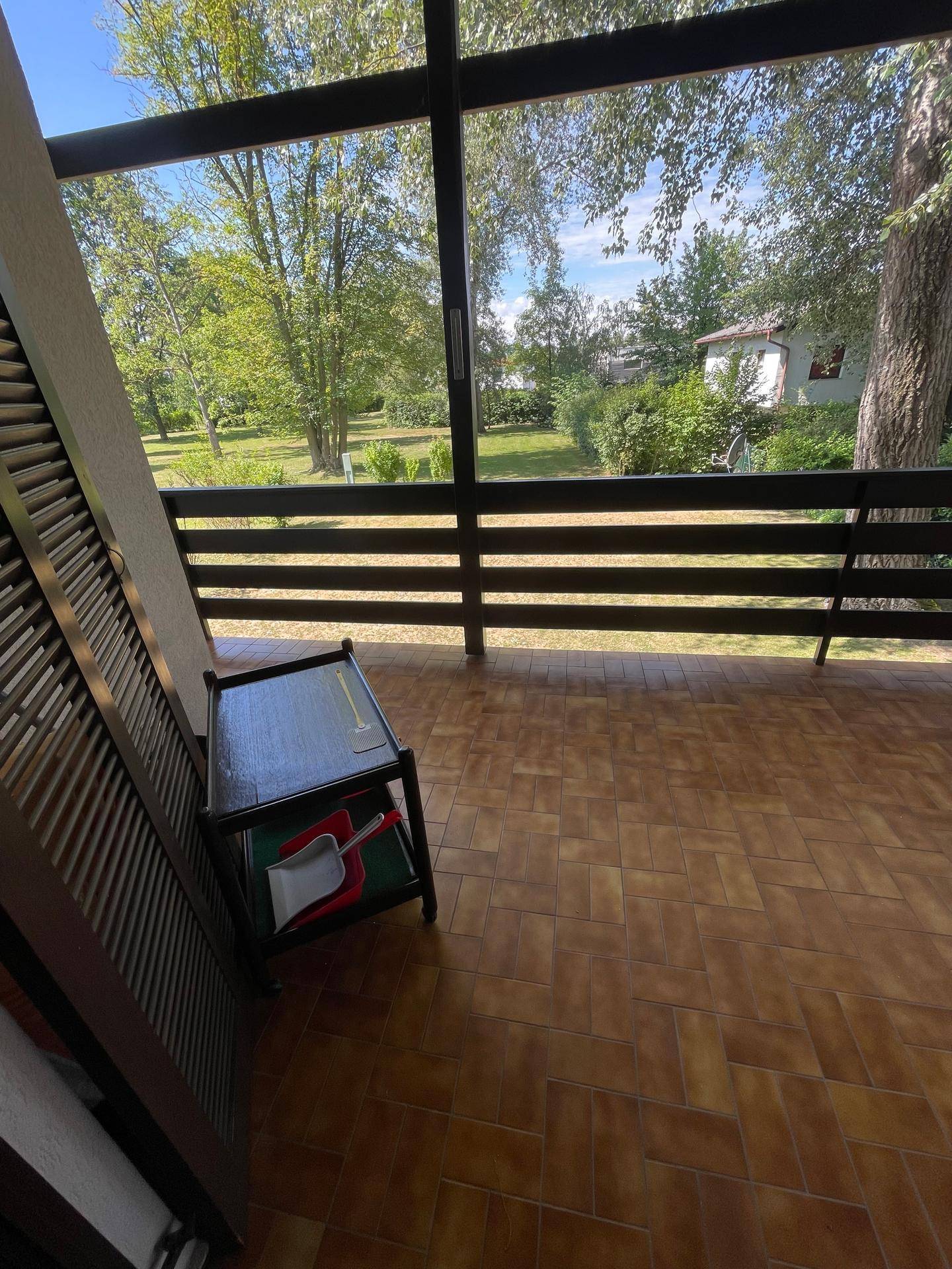 Geräumiger Balkon mit braunen Fliesen und einem kleinen Beistelltisch, umgeben von Natur.