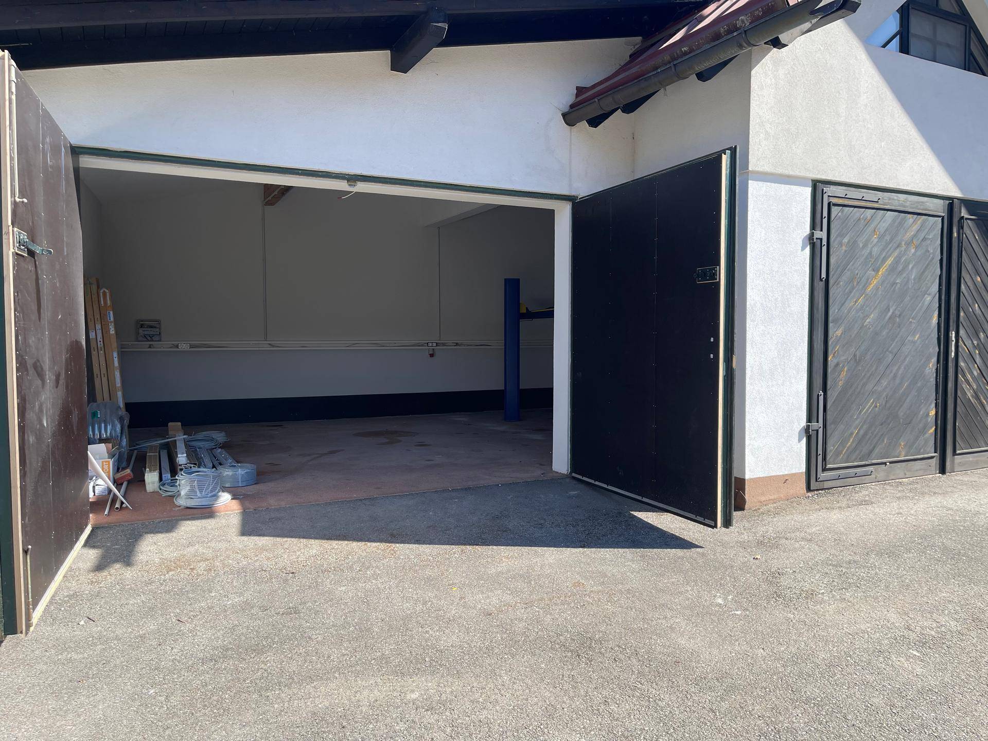 Offene Garagentür gibt den Blick auf einen geräumigen Innenraum mit Betonboden und sichtbaren Holzbalken frei.