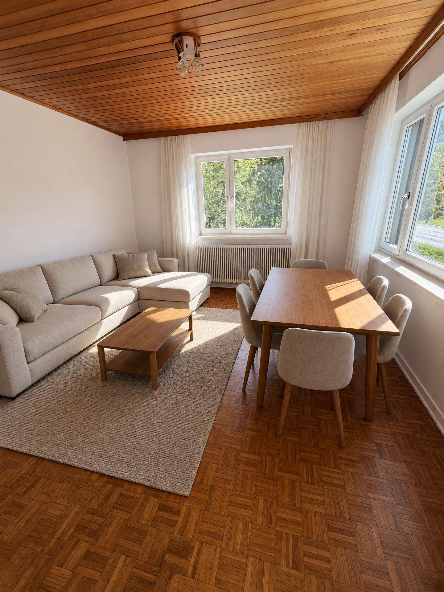 Heller Wohn-Essbereich mit Holzbalkendecke, Parkettboden und großzügigen Fenstern.