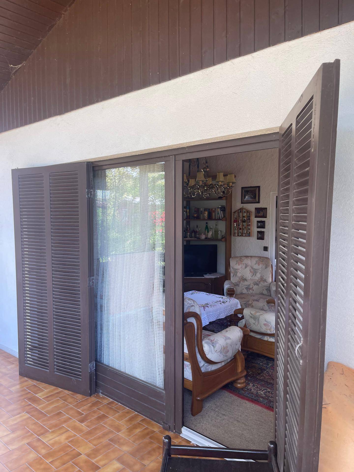 Balkon mit geöffneten Fensterläden und Blick in einen traditionell eingerichteten Wohnbereich.