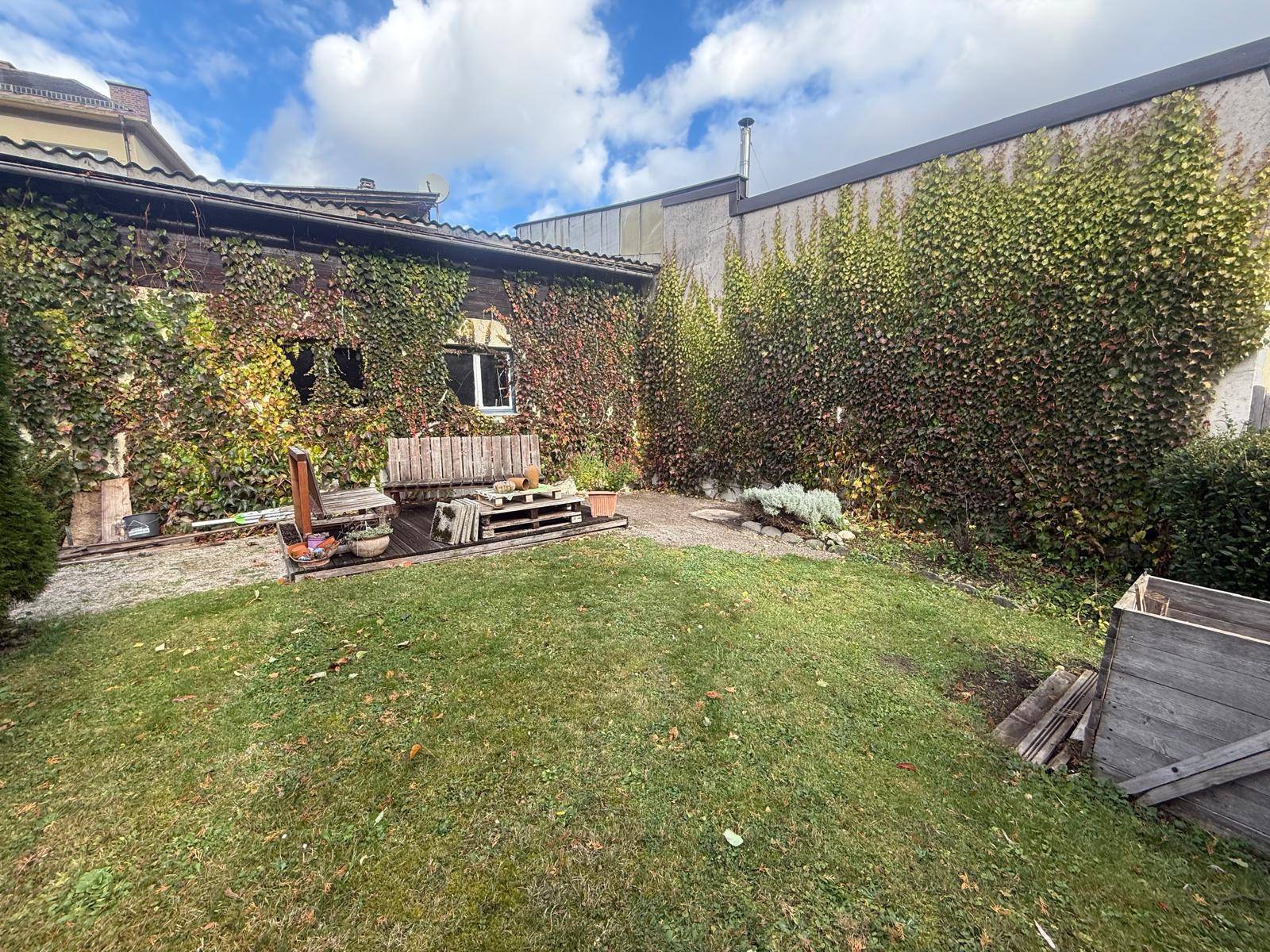 Garten mit Holzbänken und üppig bewachsenen Wänden, ideal zum Entspannen im Freien.