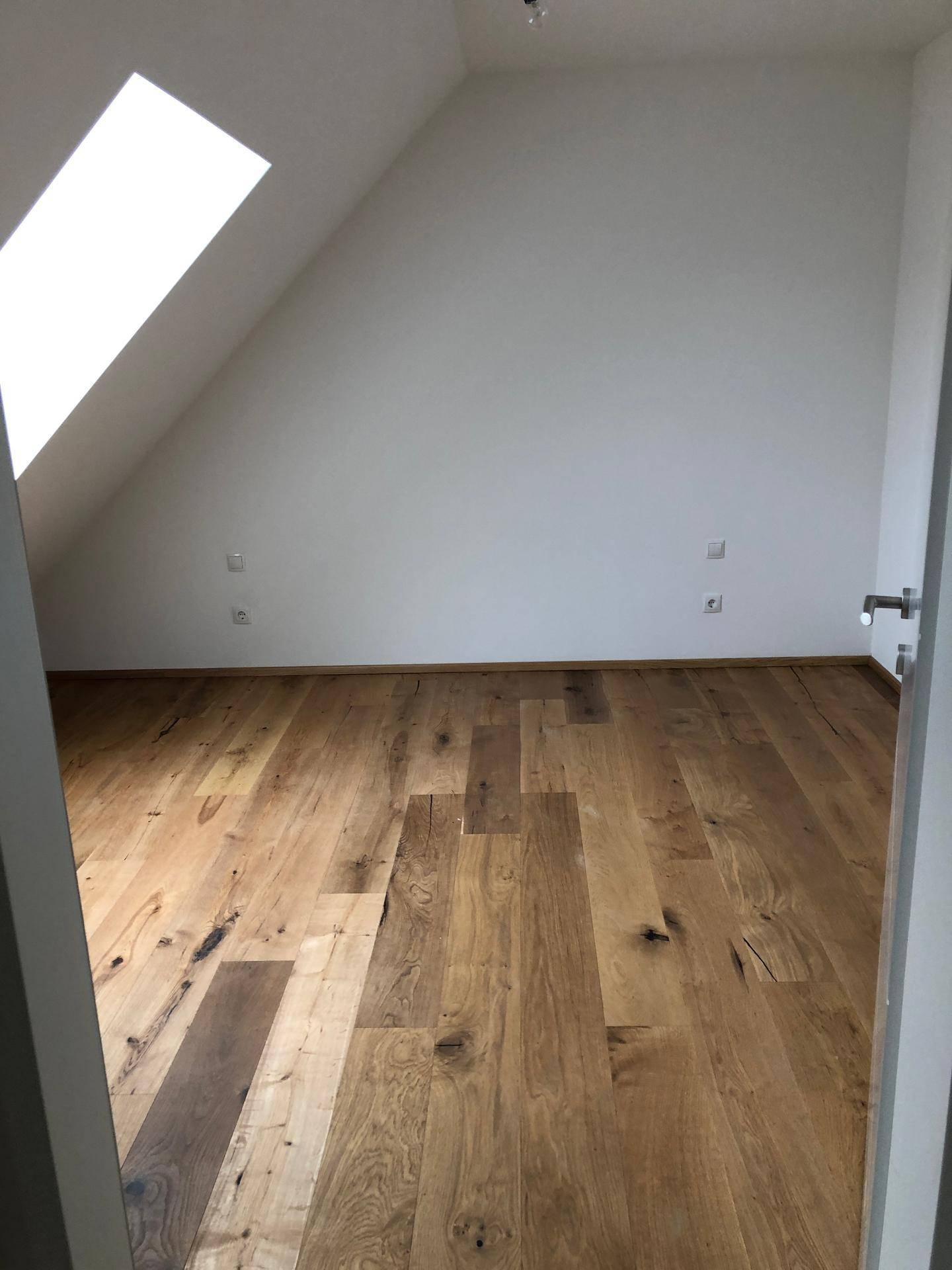 Helles Dachgeschosszimmer mit Holzboden und schräger Decke, ideal für ein Schlafzimmer.