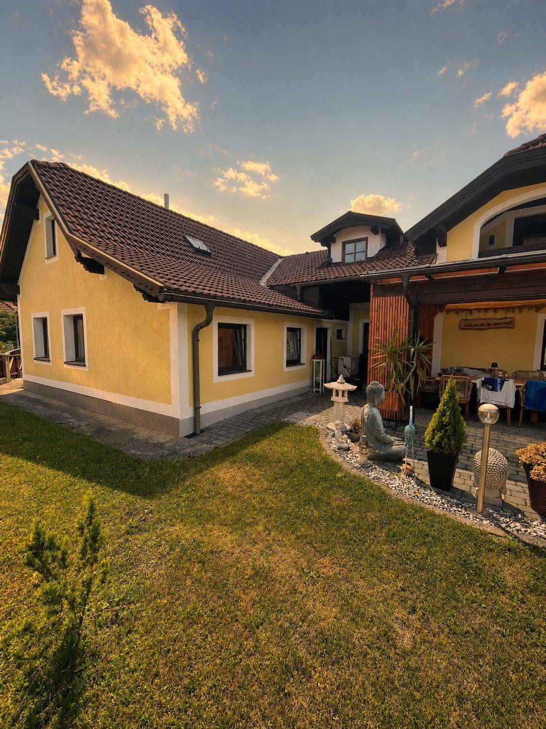 Gelbes Haus mit rotem Dach und gepflegtem Gartenbereich unter einem bewölkten Himmel, sehr einladend.