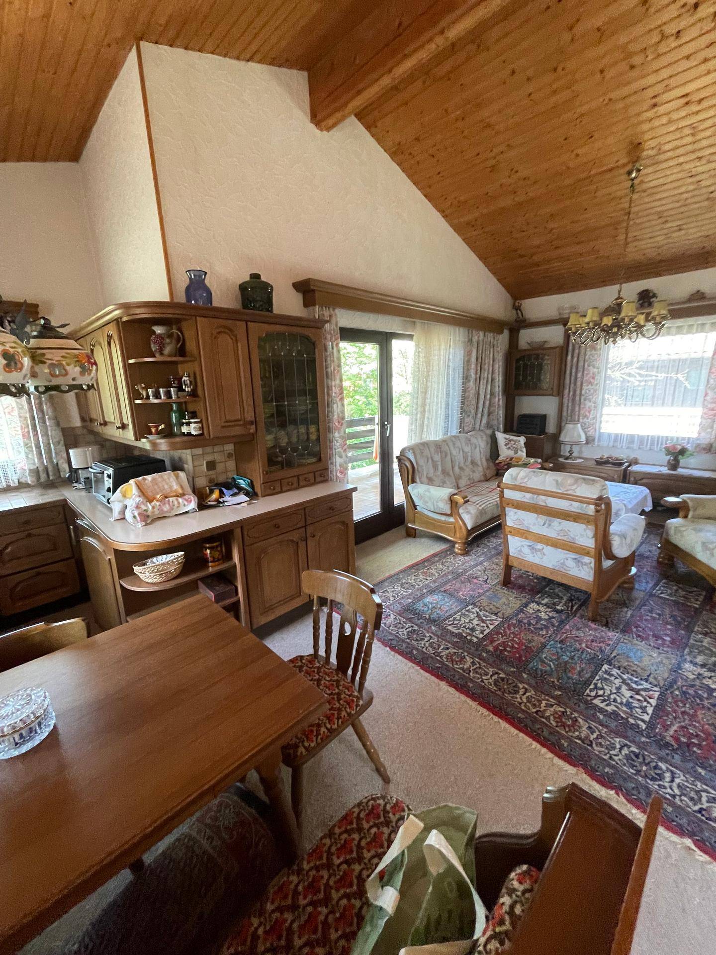 Traditionelle Wohnküche mit dunklen Holzmöbeln, Essbereich und Zugang zum Balkon.