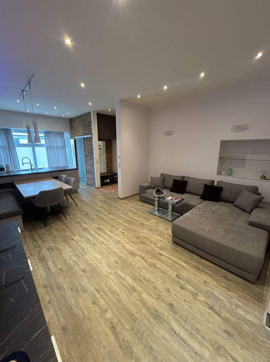 Gemütliches Wohnzimmer mit großem Ecksofa, Holzboden und offener Verbindung zur Küche.