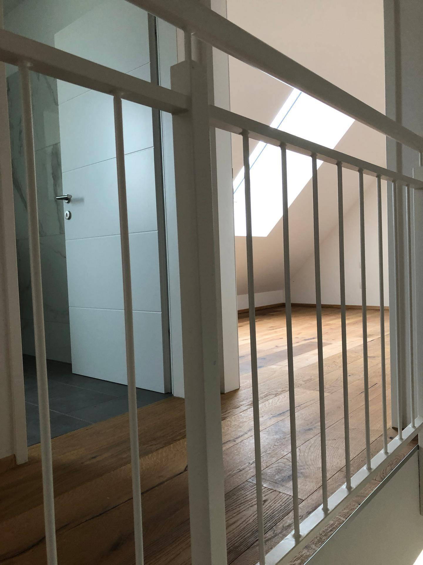 Heller Flur im Obergeschoss mit Treppengeländer und Zugang zu einem Zimmer mit Dachfenster.